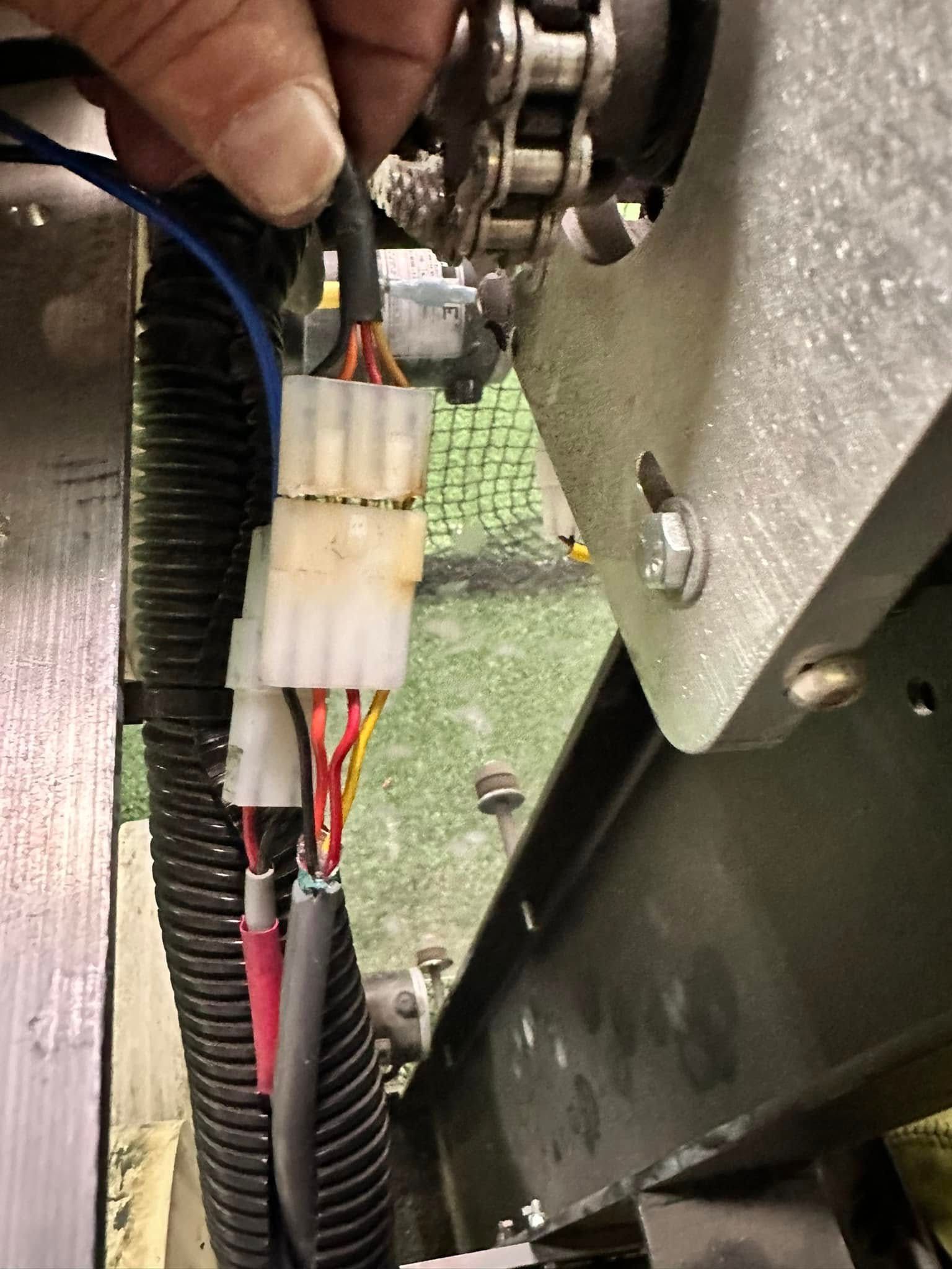Close-up of electrical wiring and connector inside a machine, with a hand holding the cable bundle.