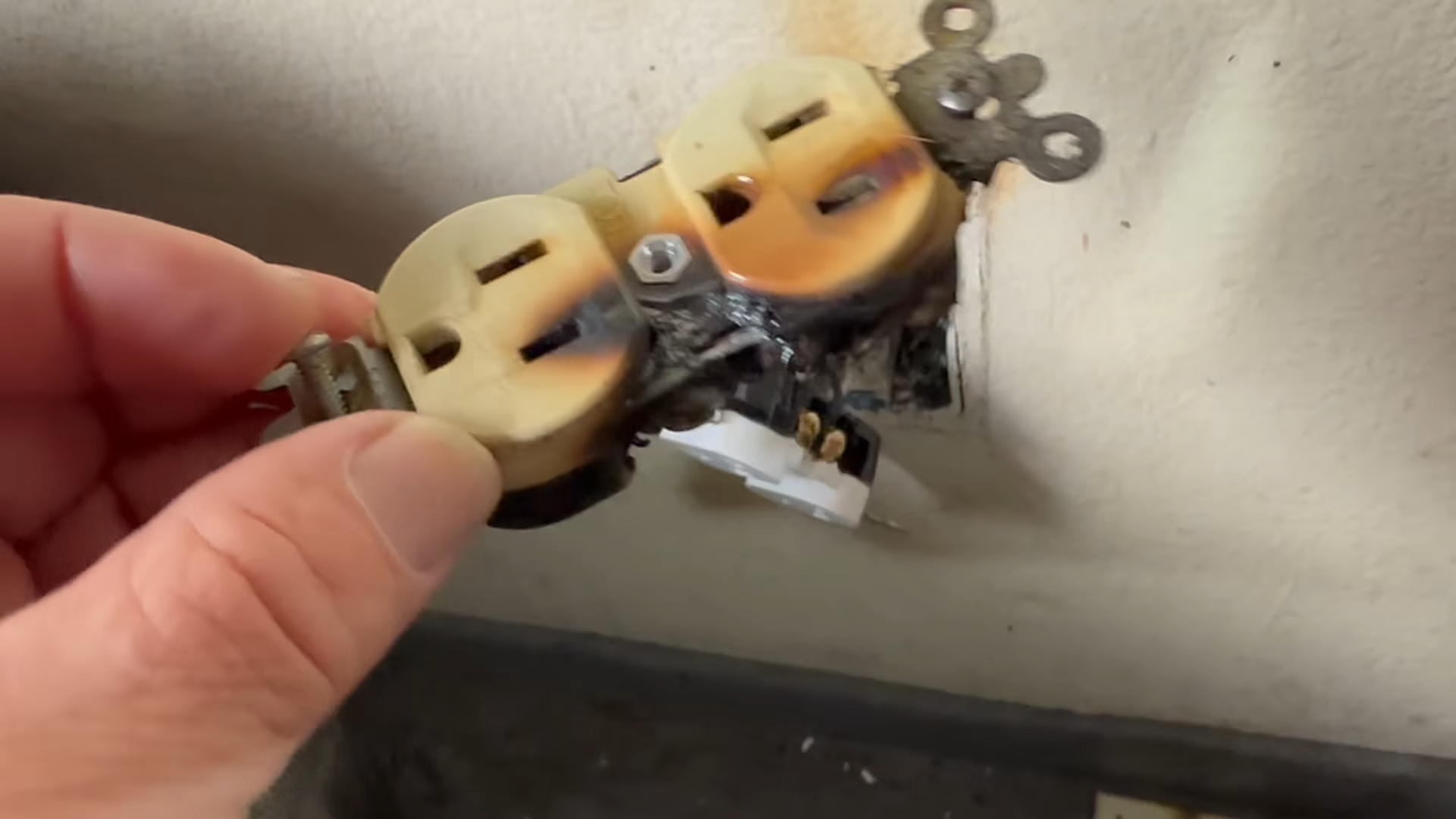 Hand plugging a worn duplex electrical outlet into a wall