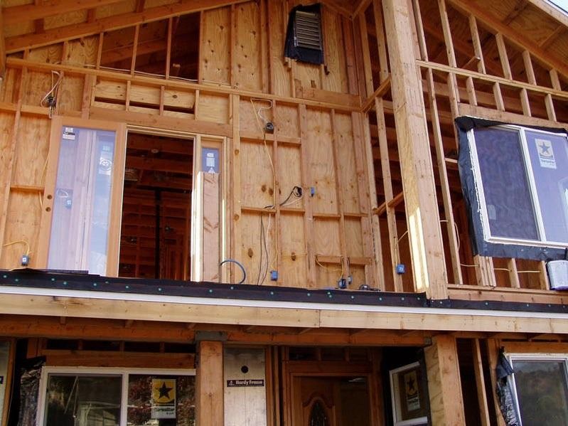 Partially built wooden house exterior with exposed framing and blue housewrap panels