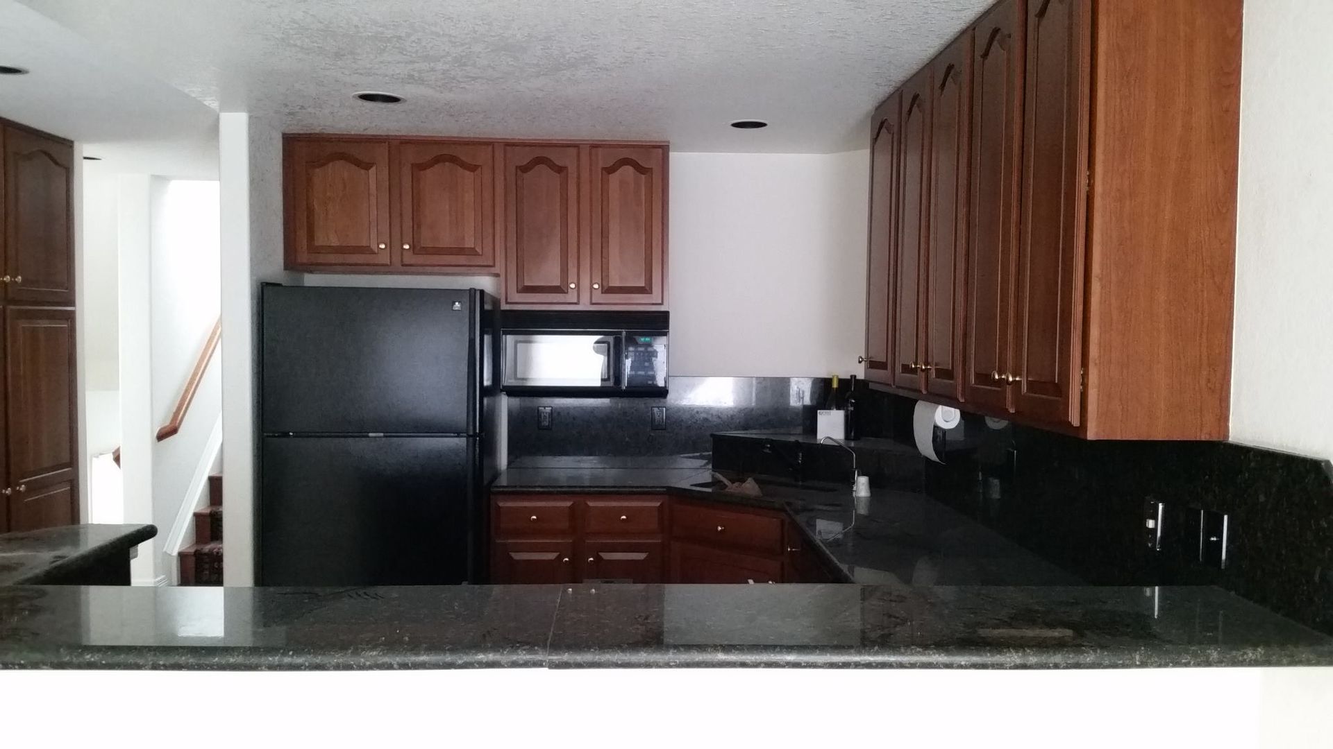 Modern kitchen with wooden cabinets and black refrigerator.