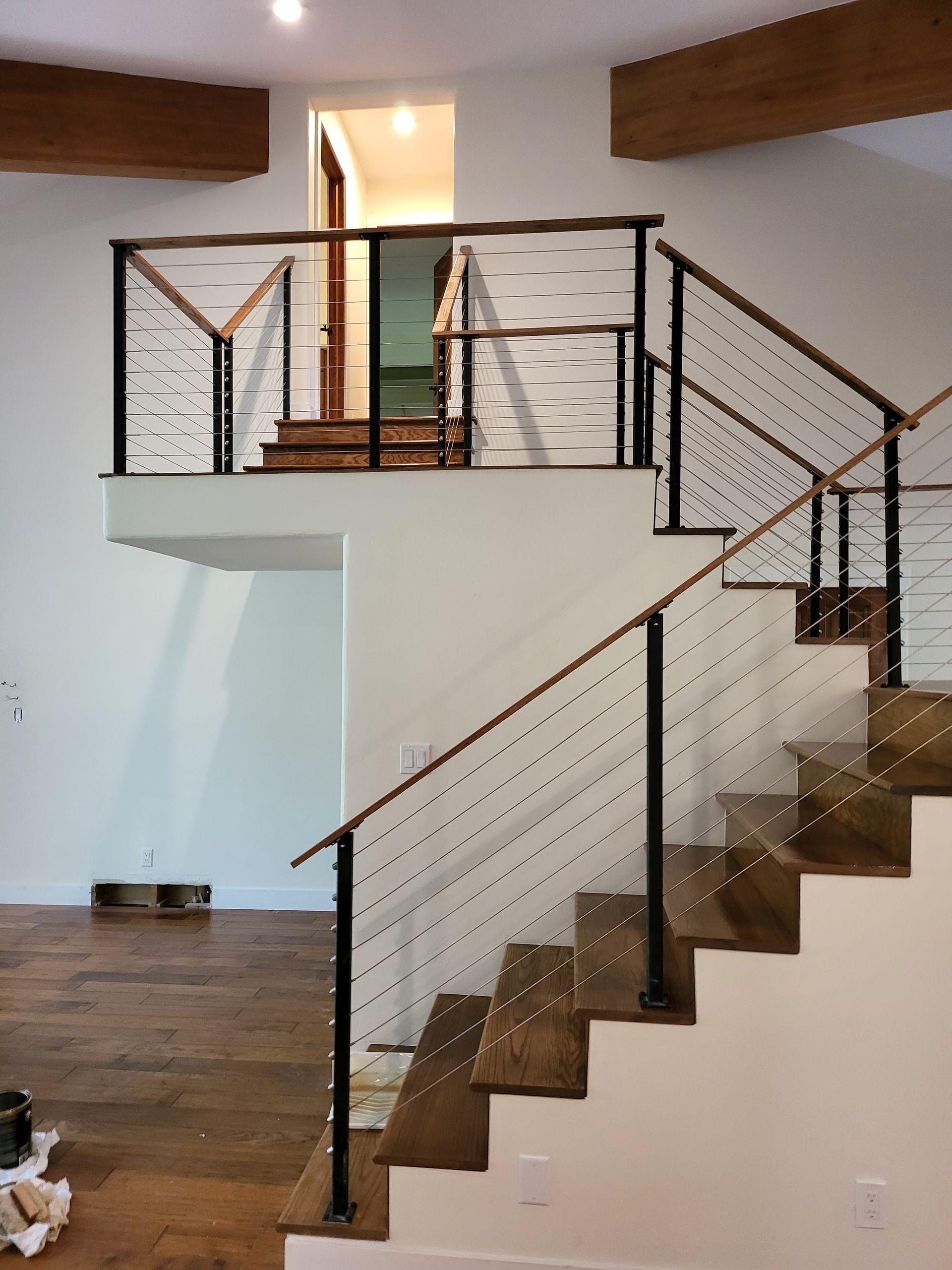 Modern wood staircase renovation with metal cable railing and open landing design.
