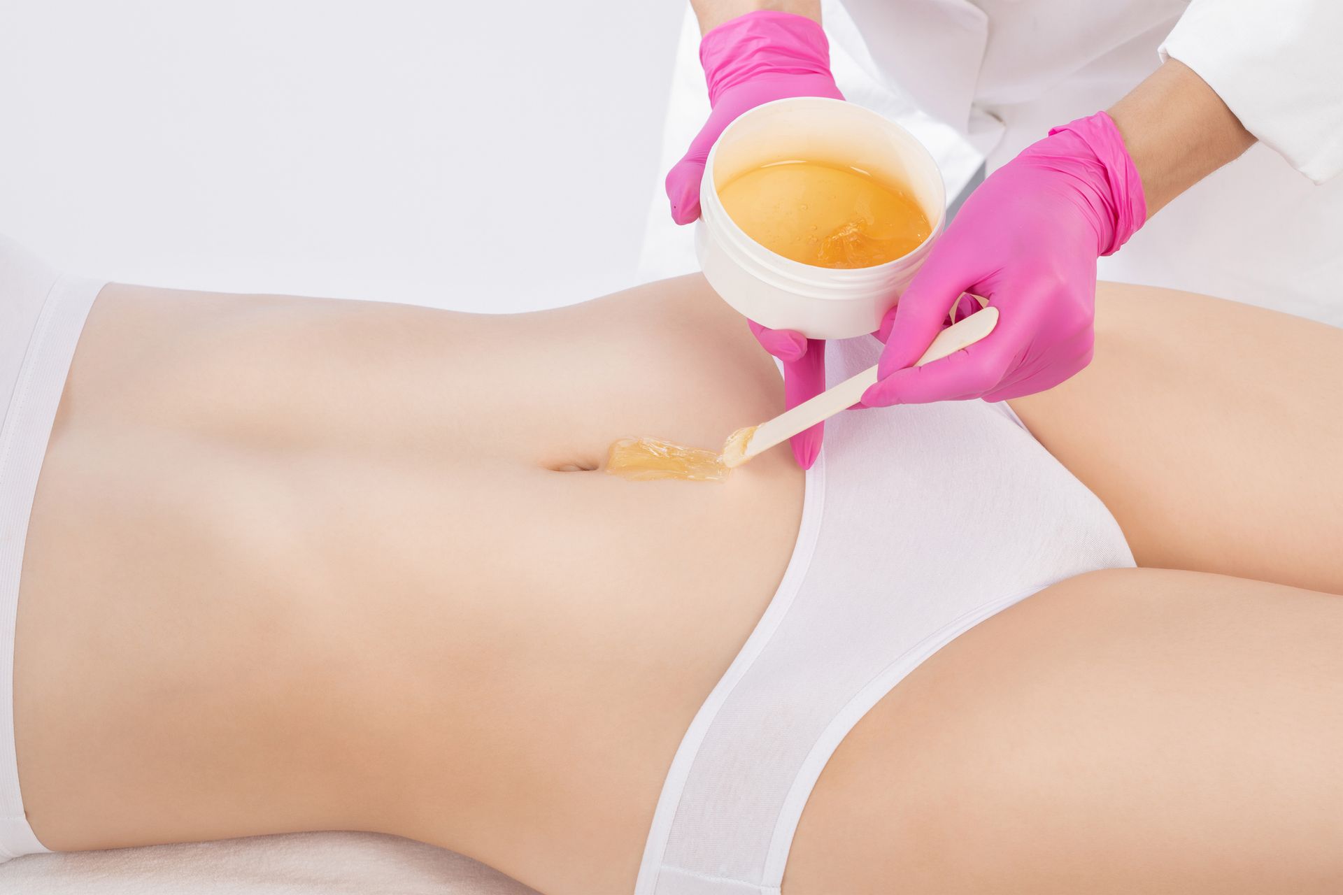 Person getting abdominal waxing treatment, with gloved hands applying wax to the lower abdomen.