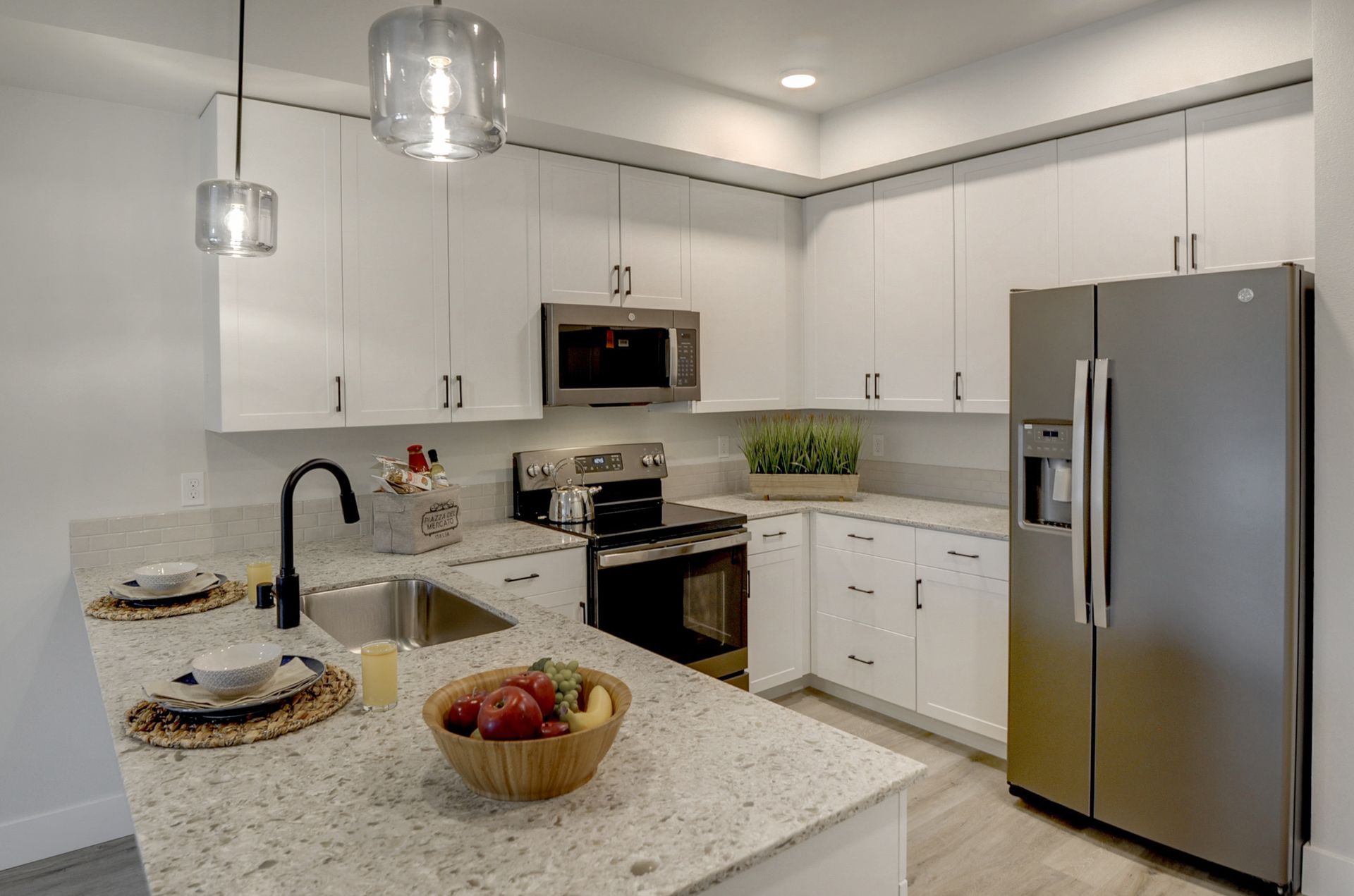 a kitchen with white cabinets , a stainless steel refrigerator , a sink , and a microwave .