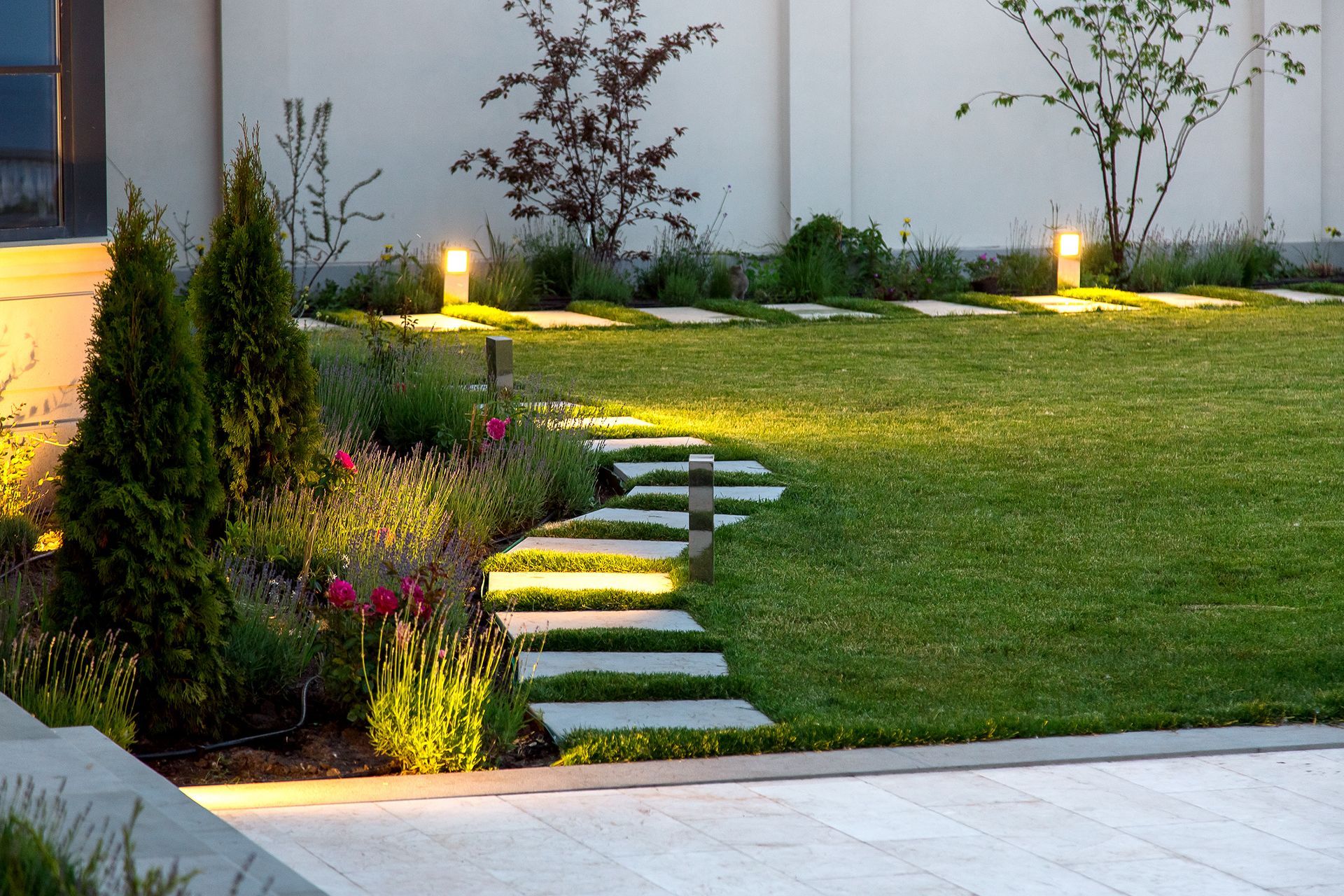 Lush garden at night with illuminated pathway lights, grass, and various plants. Lush garden at night with glowing pathway lights illuminating plants, trees, and lawn.