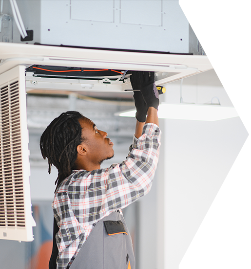 HVAC technician in gray overalls and gloves, repairing ceiling unit. HVAC technician working on ceiling unit. Wearing gloves and a plaid shirt.