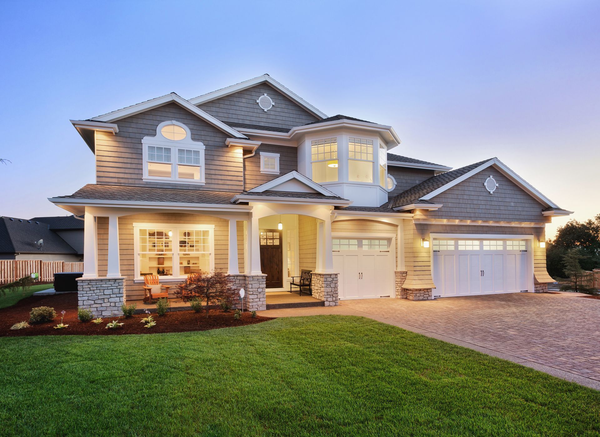 Two-story house with gray siding, white trim, and a manicured lawn at dusk. Two-story gray house with white trim, a gabled roof, and a green lawn at dusk.