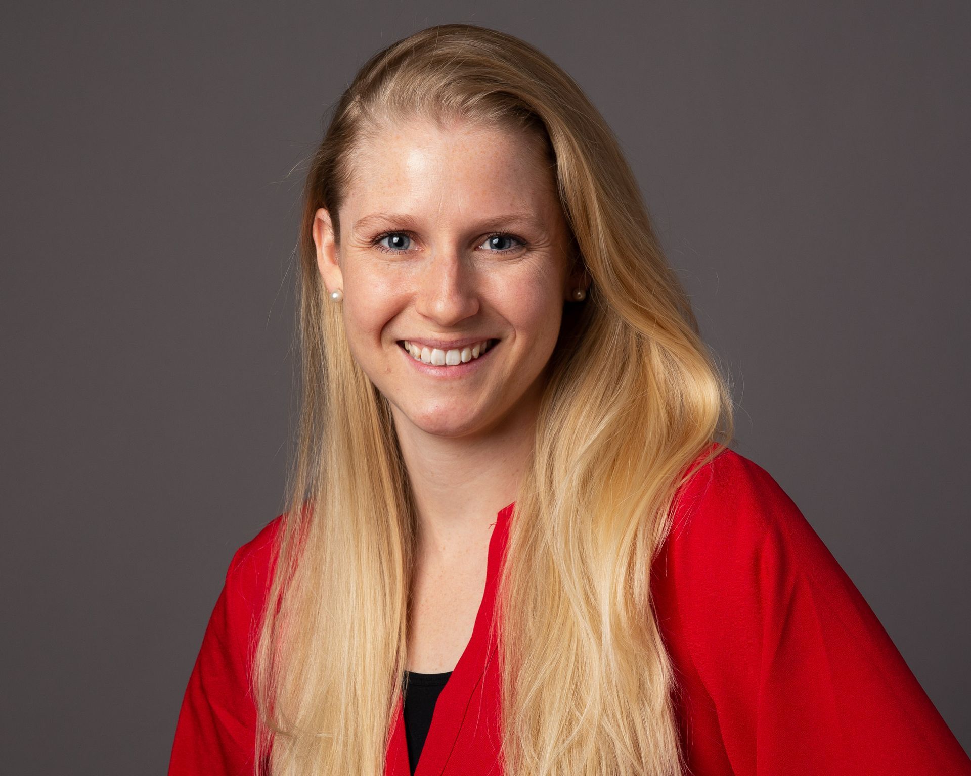 A woman with long blonde hair is wearing a red shirt and smiling.