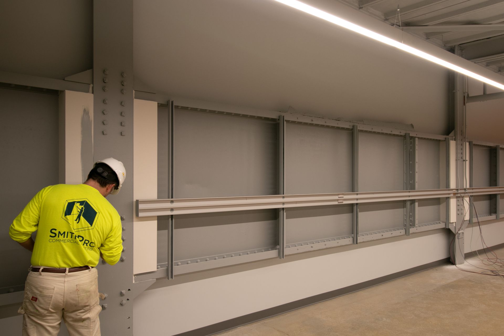 SmithPro Worker in a neon yellow shirt, painting a wall-mounted shelf in an unfinished room.