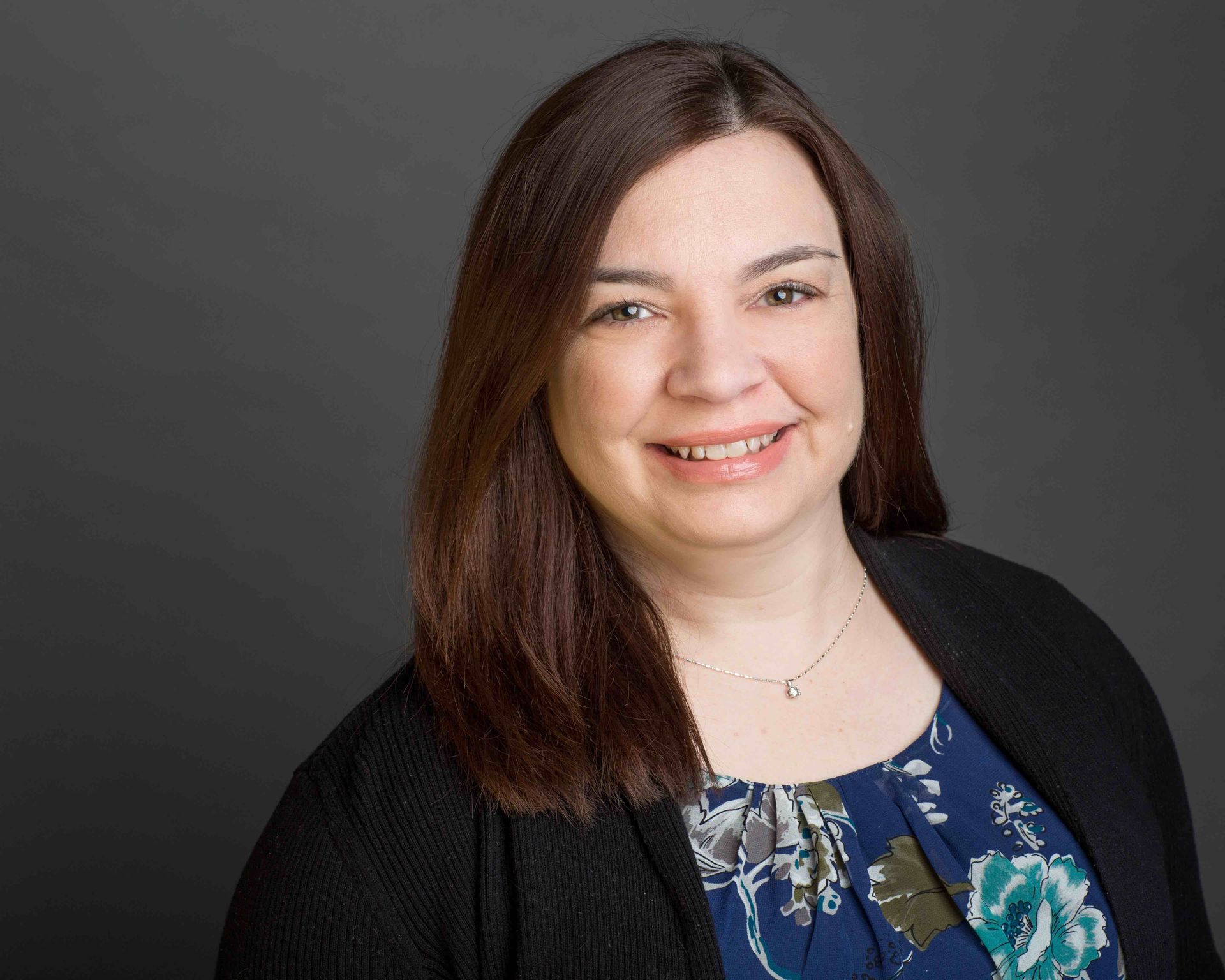 A woman is smiling for the camera while wearing a black sweater and a floral shirt.