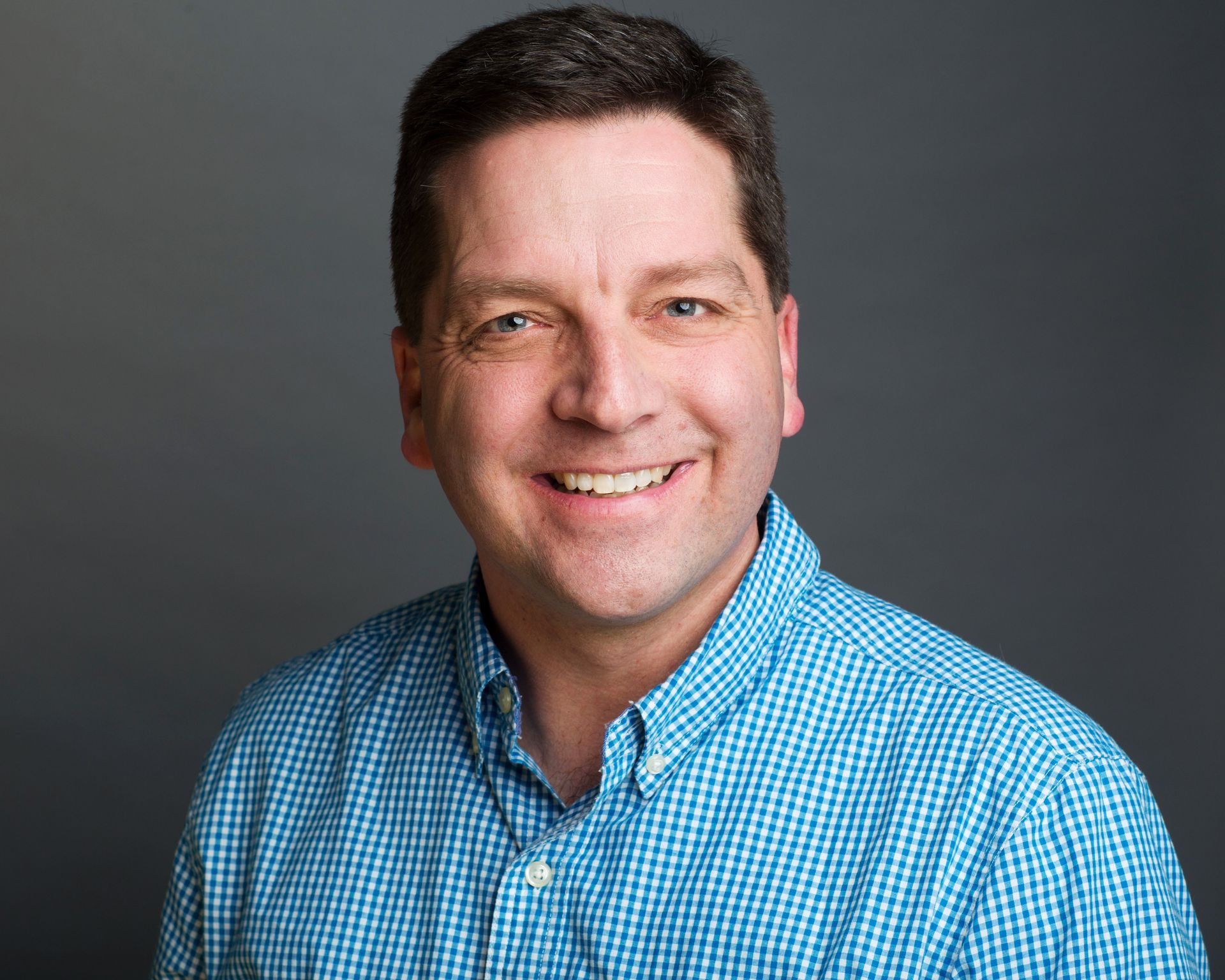 A man in a blue plaid shirt is smiling for the camera.