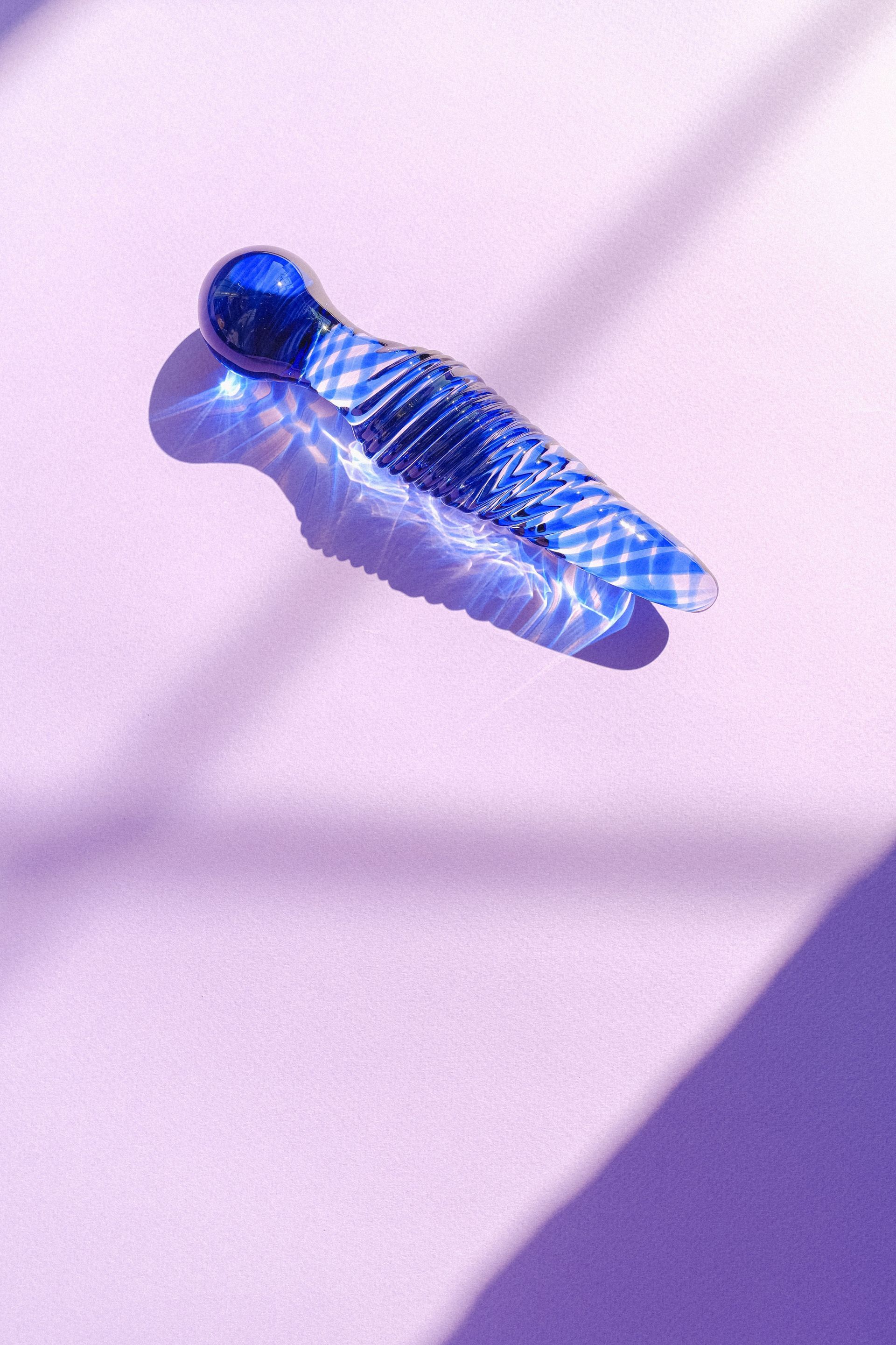 Figura de cristal azul sobre una superficie rosa pálido, iluminada por suaves sombras diagonales.