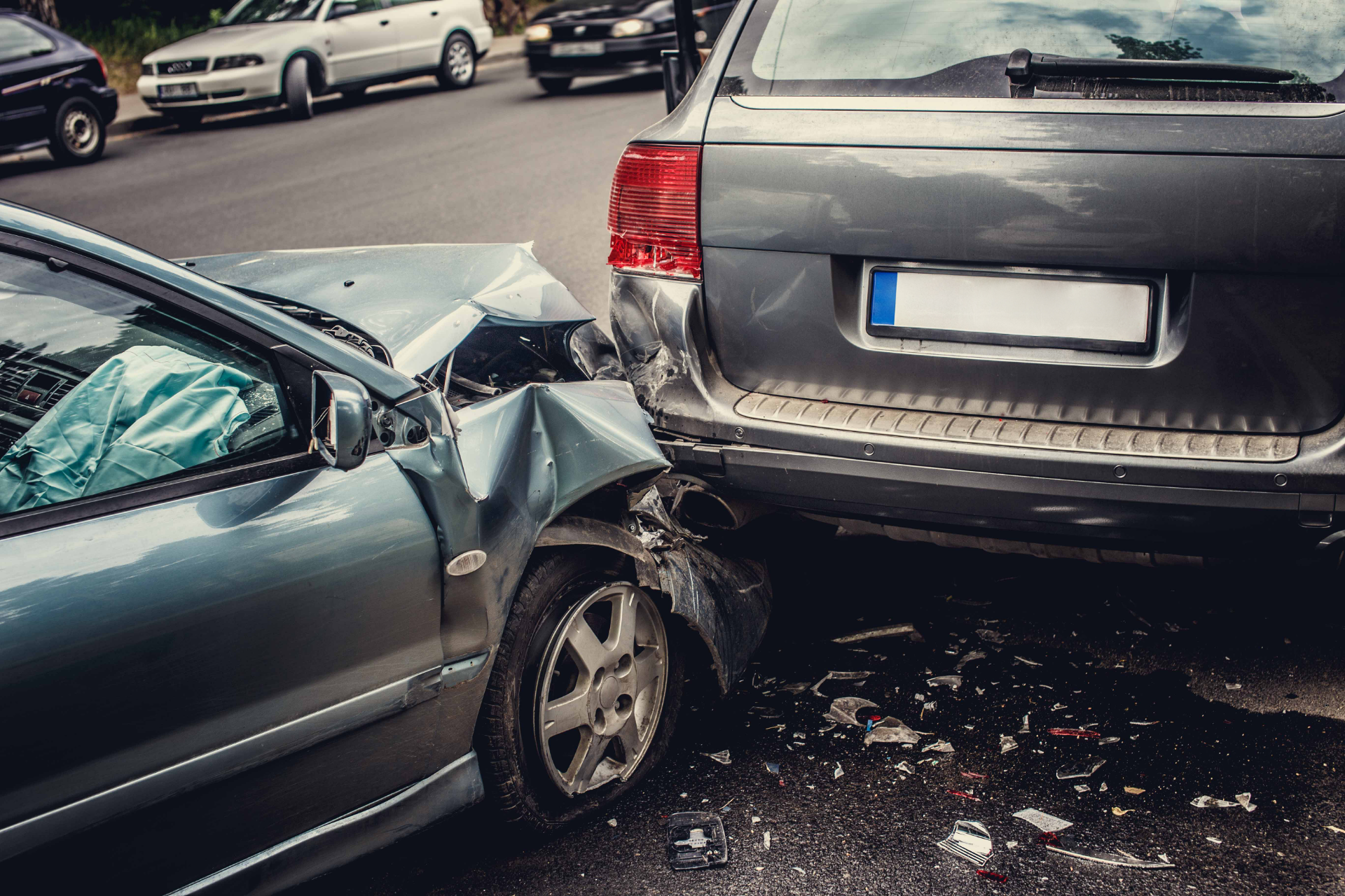 Cars involved in a rear-end collision on a city street; gray car hit by a blue car, airbags deployed.