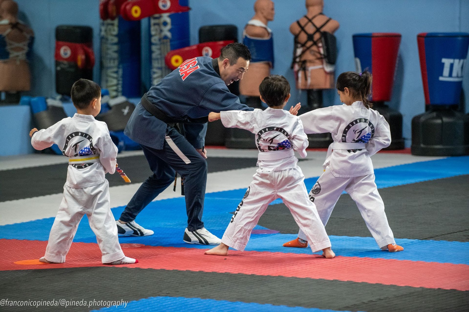 A group of young boys are practicing martial arts with a man in a gym.