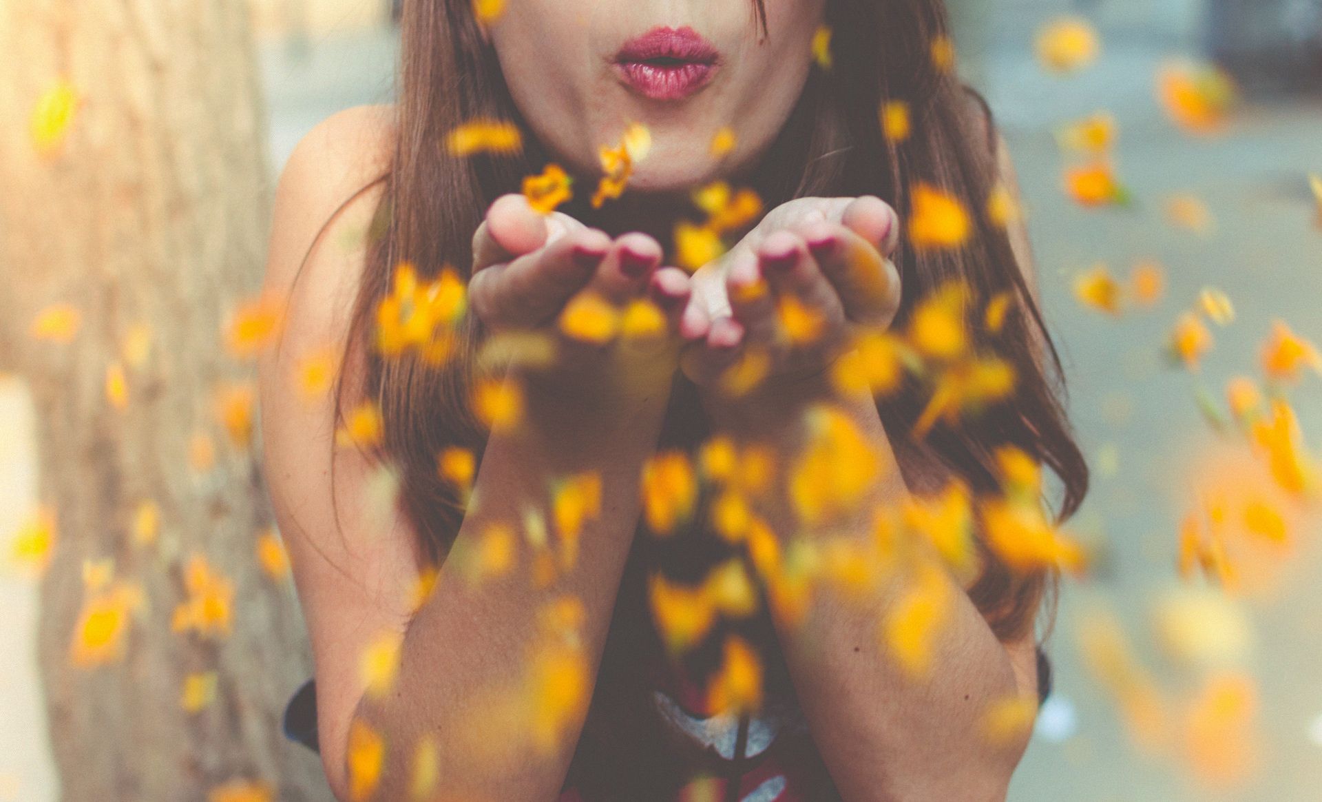 A woman is blowing leaves out of her hands.