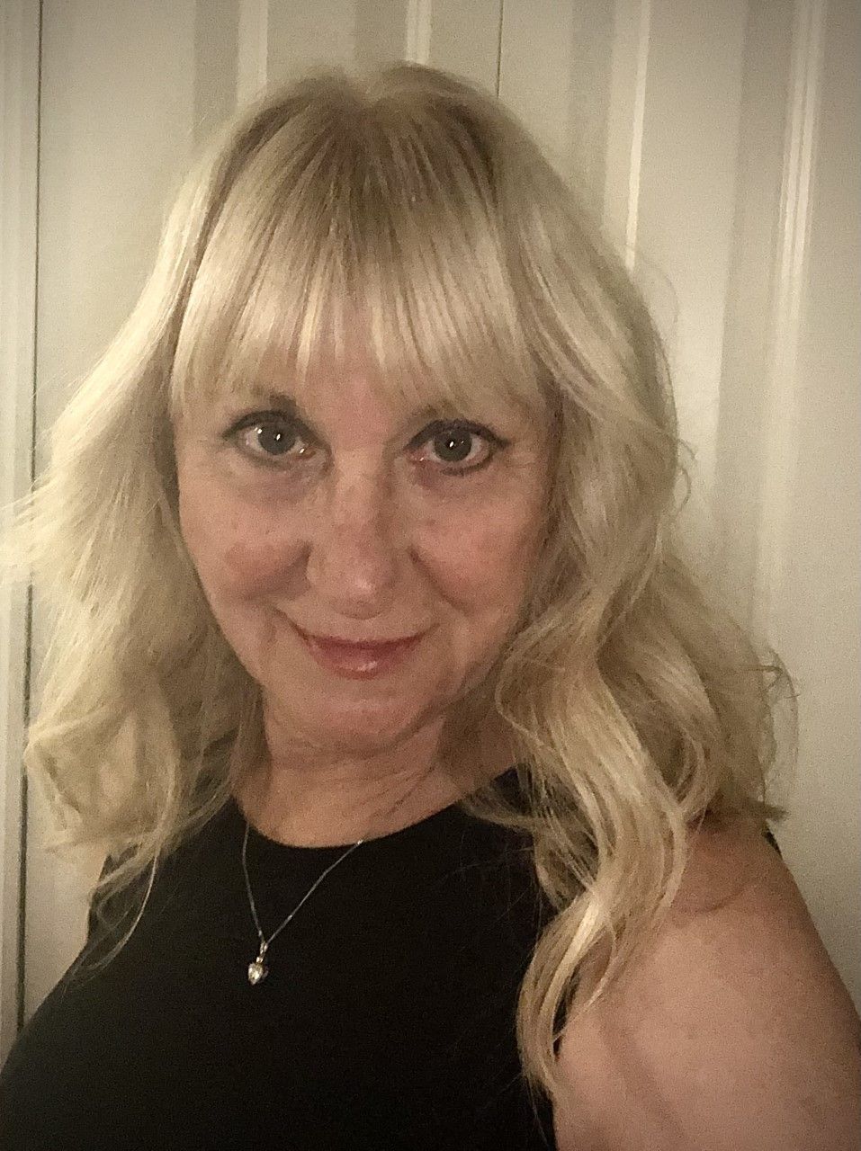 A woman with blonde hair is wearing a black dress and a necklace.