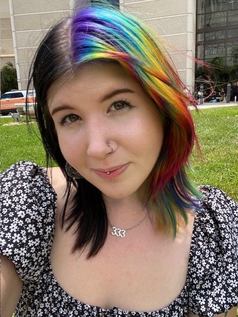 A woman with rainbow hair is wearing a necklace with the number 333 on it