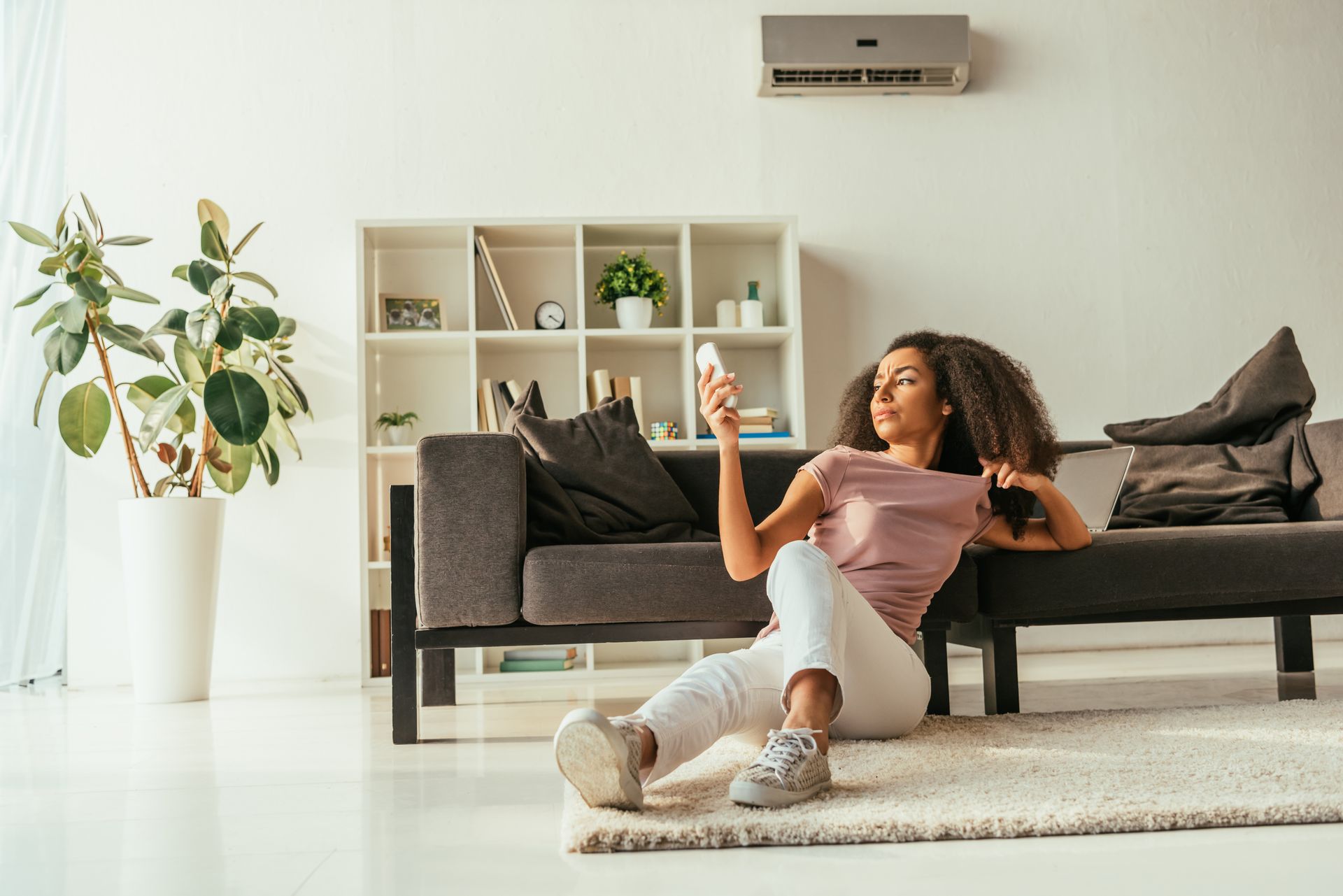 A woman is sitting on the floor in a living room holding a remote control.