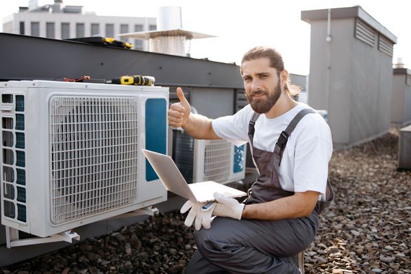 A man is sitting on a roof with a laptop and giving a thumbs up.