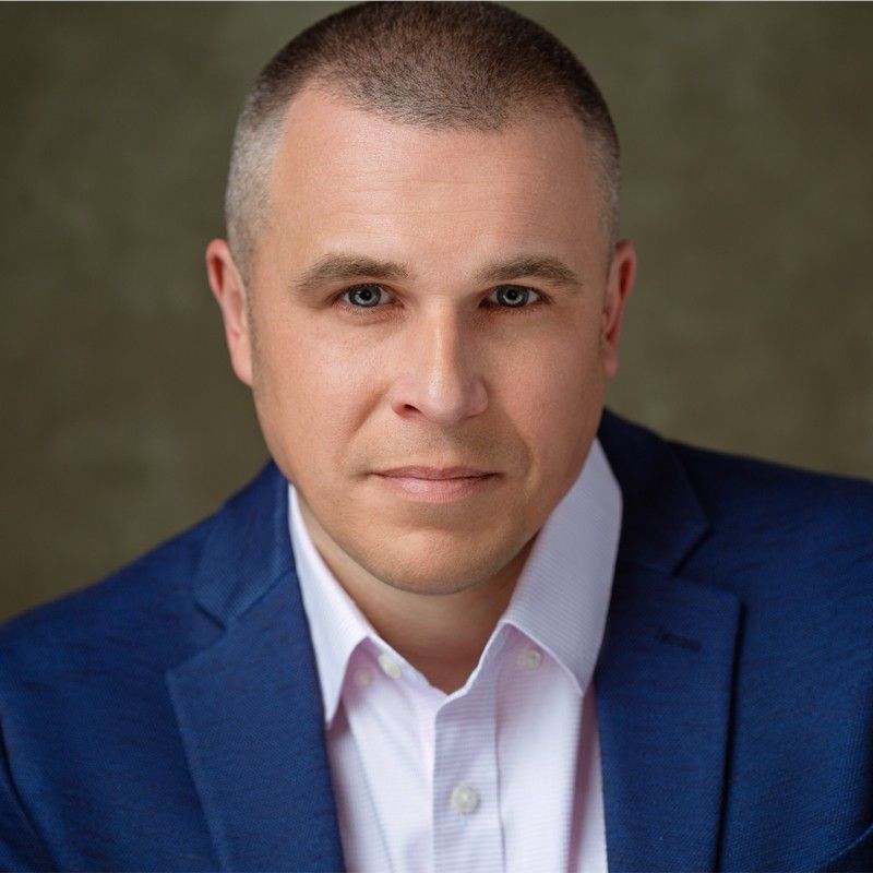 Man in blue suit, light pink shirt, looking at the camera.