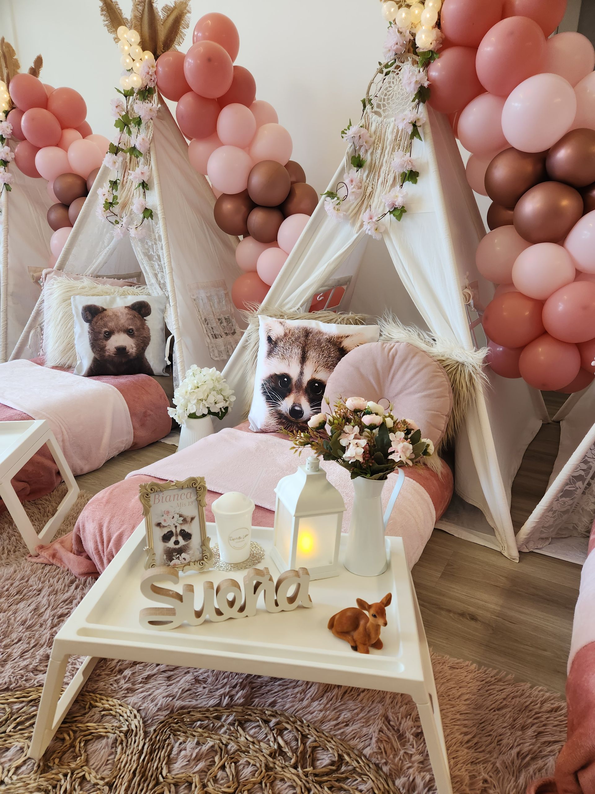 Fiesta glamping en interiores con tipis, globos rosas y almohadas con forma de animales.