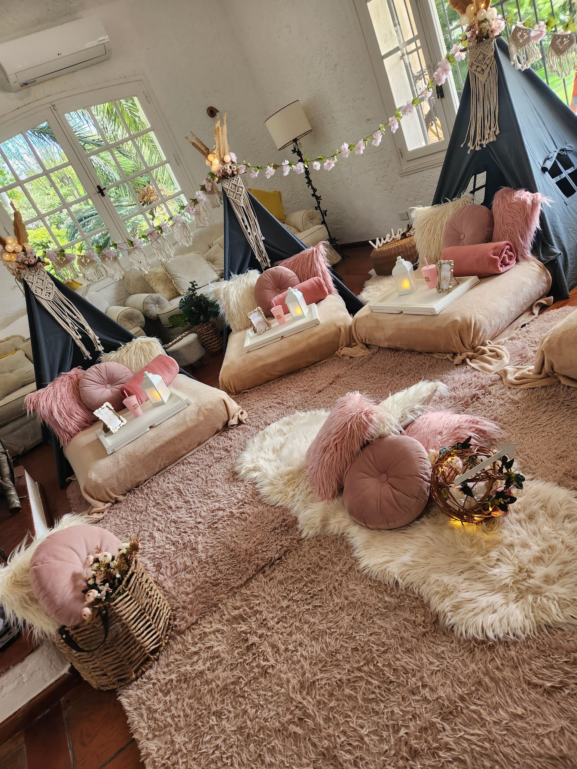 Acogedor montaje para fiesta de pijamas en interiores con tipis, almohadas rosas, alfombras y decoraciones.