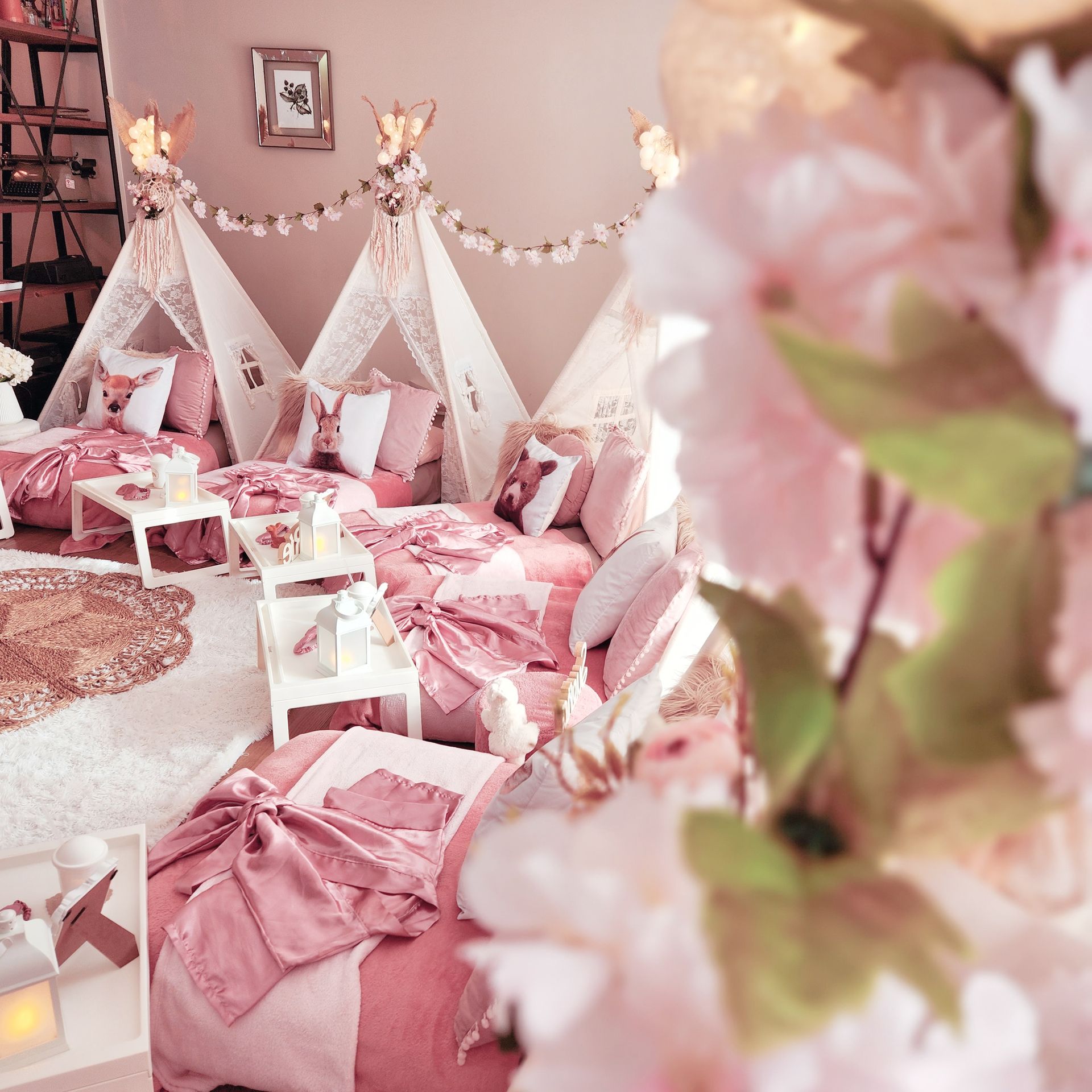 Dormitorio rosa con tipis, almohadas y flores decorativas.