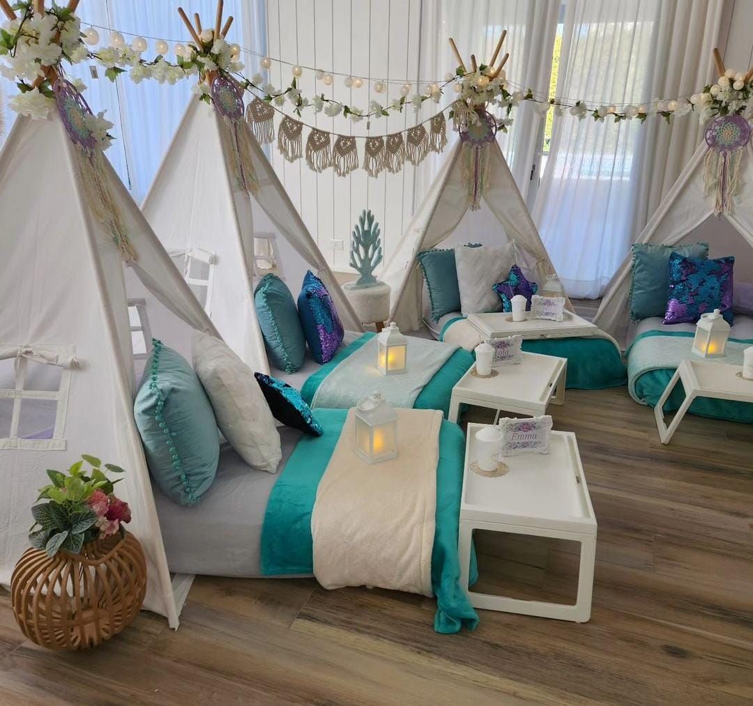 Tiendas tipi decoradas con mantas turquesas y blancas, almohadas, flores y mesas pequeñas, preparadas para una fiesta.