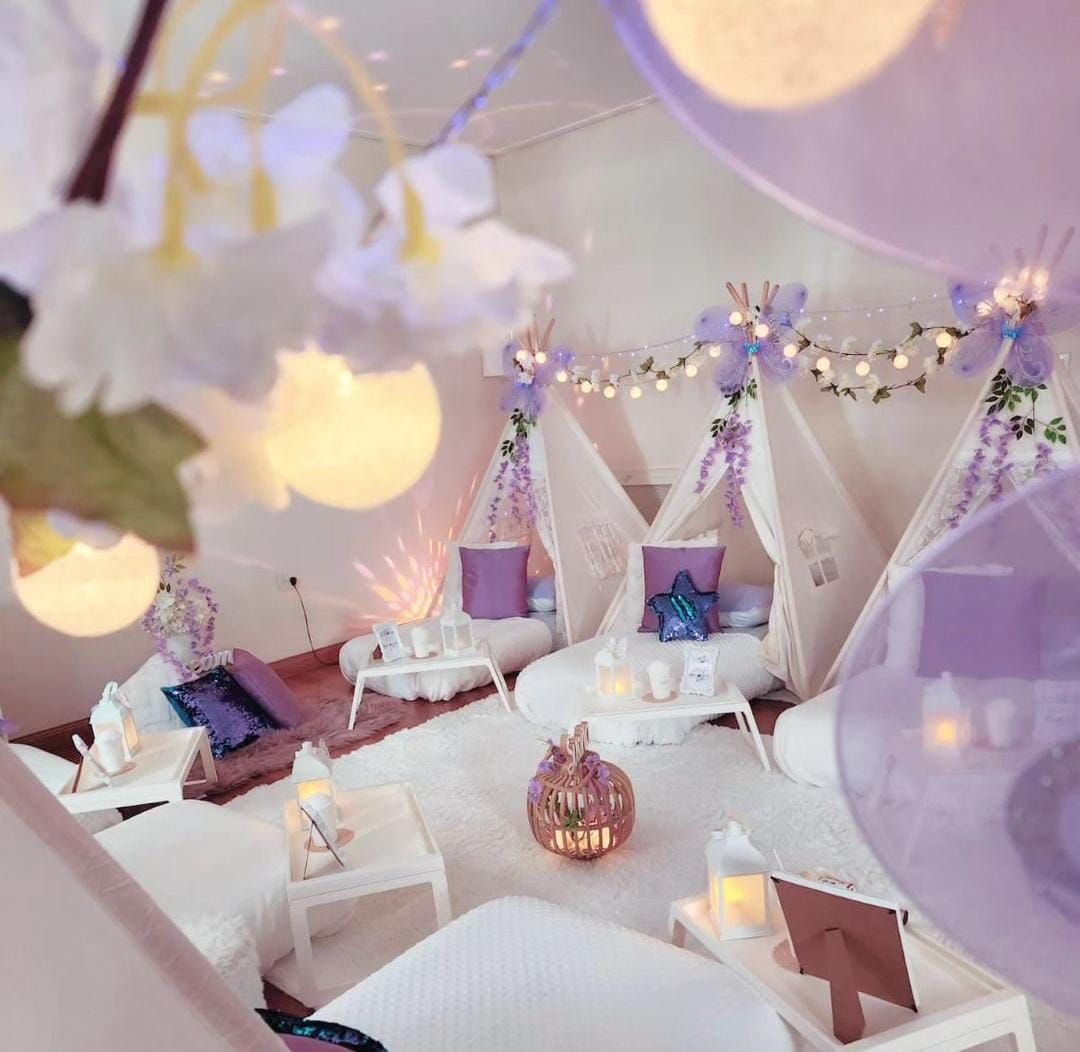 Acogedor entorno para una pijamada con tipis, alfombras blancas, decoración violeta y luces de colores en una habitación.
