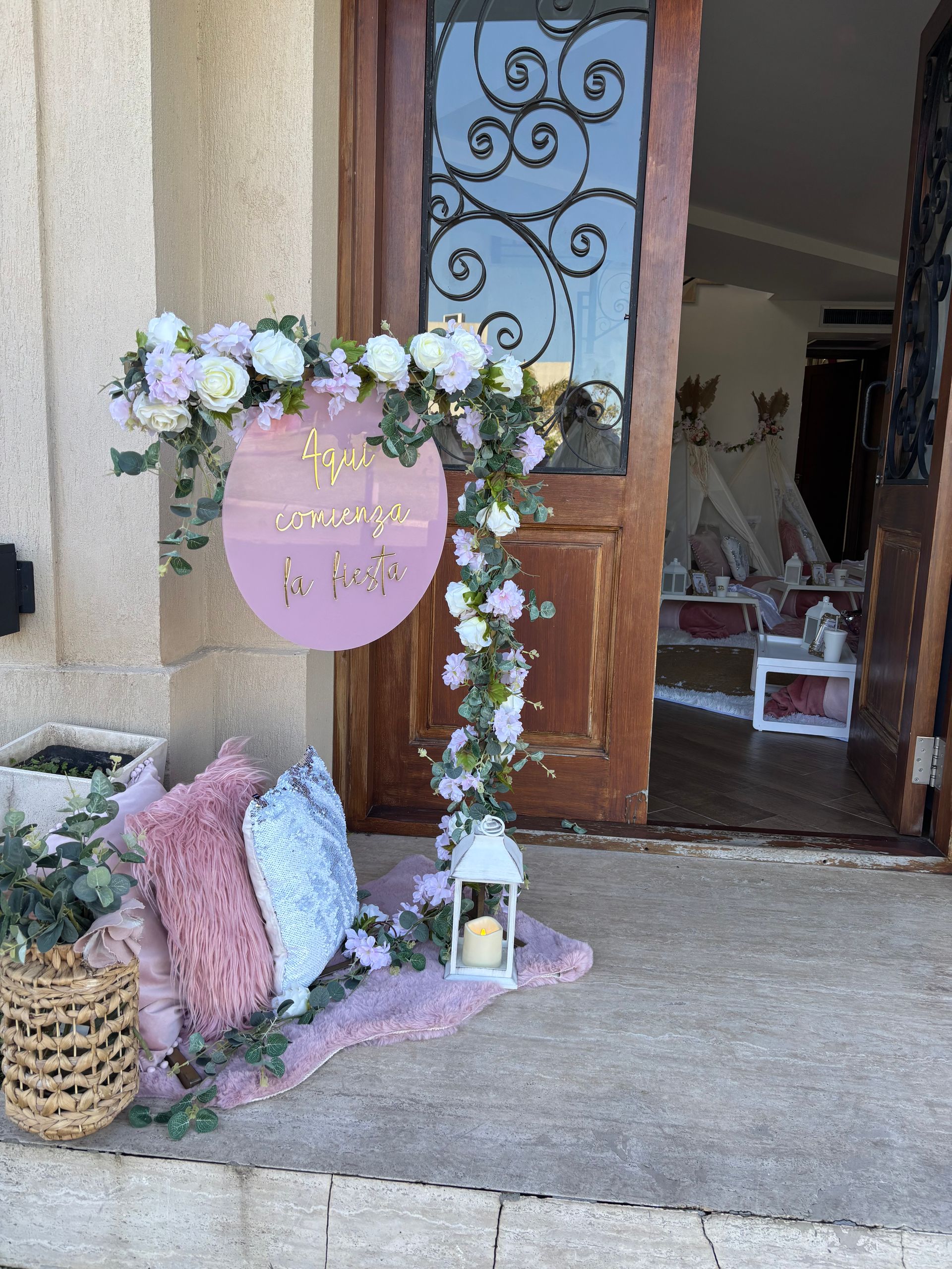Un cartel decorativo con detalles florales y una linterna afuera de una puerta, con almohadas y una alfombra en el suelo.