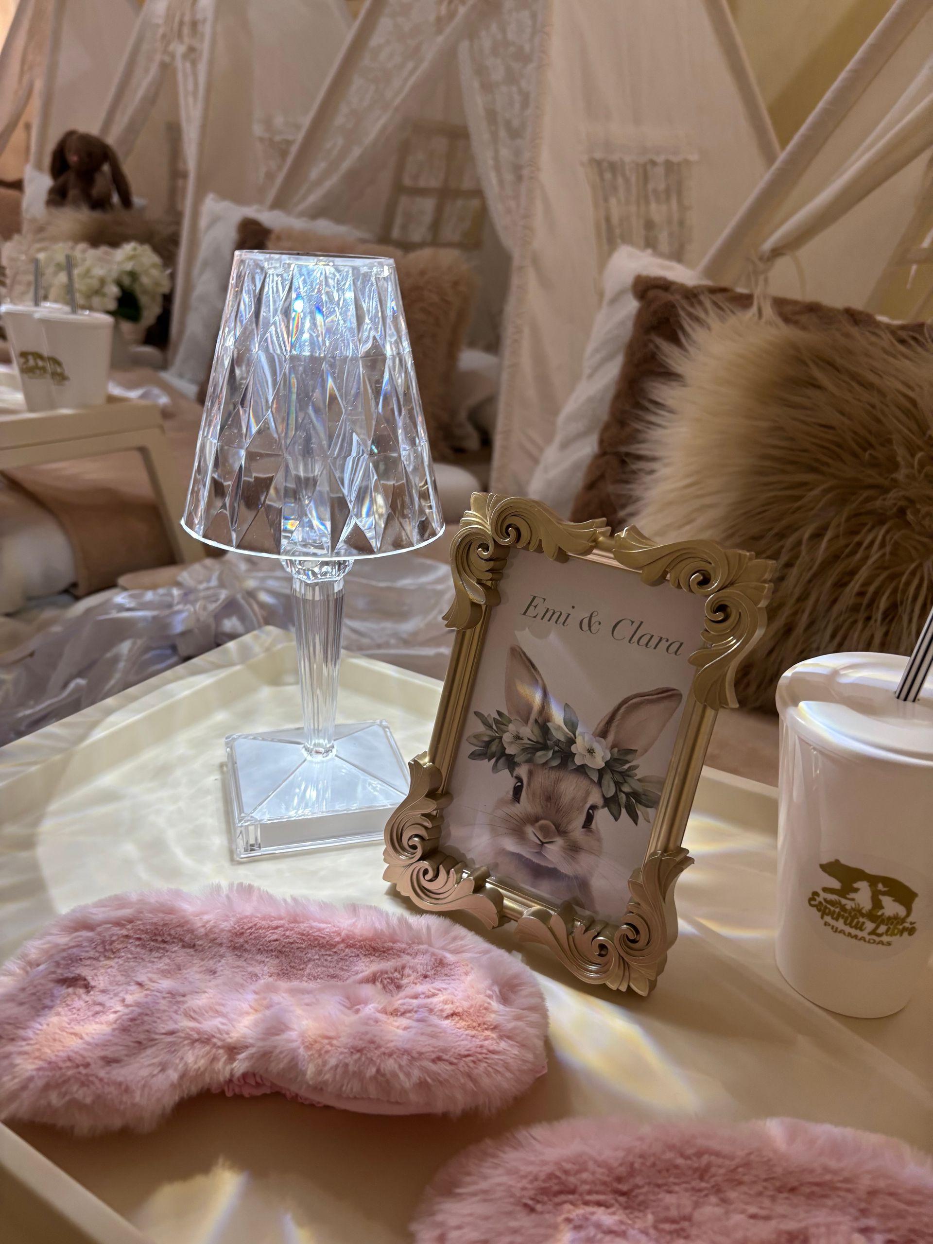 Naturaleza muerta con lámpara de cristal encendida, foto enmarcada, antifaz de piel rosa y una taza.