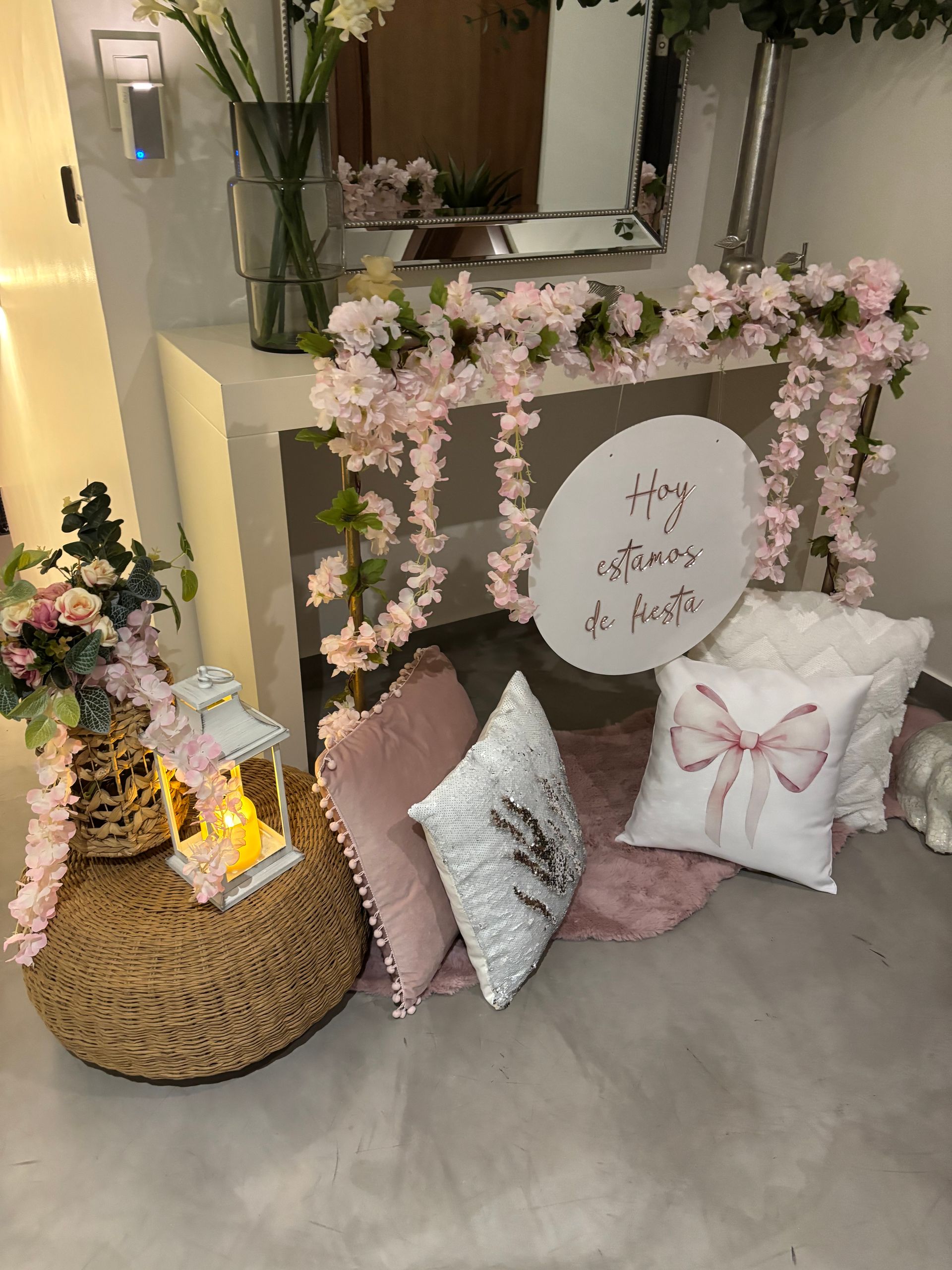 Acogedora escena interior con decoraciones florales rosas y blancas alrededor de una chimenea y almohadas en el suelo.