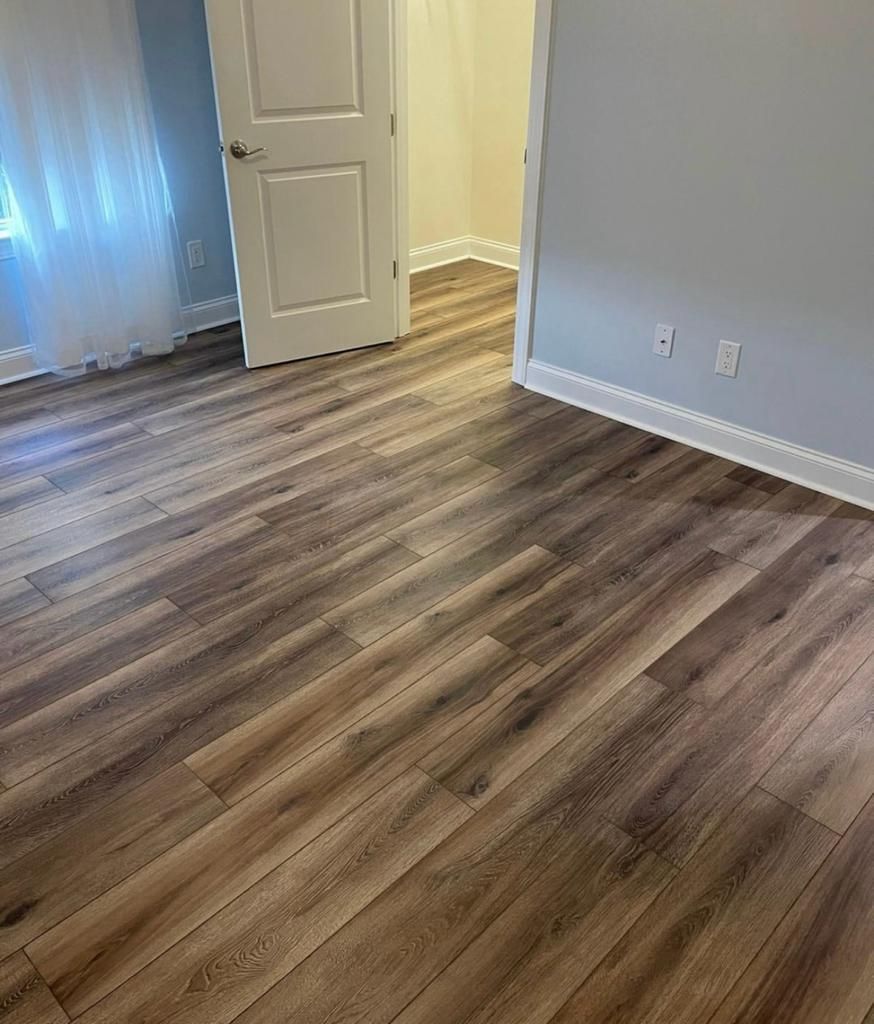 An interior view of a room with light grey walls, white trim, and wood-look laminate flooring leading to an open door.