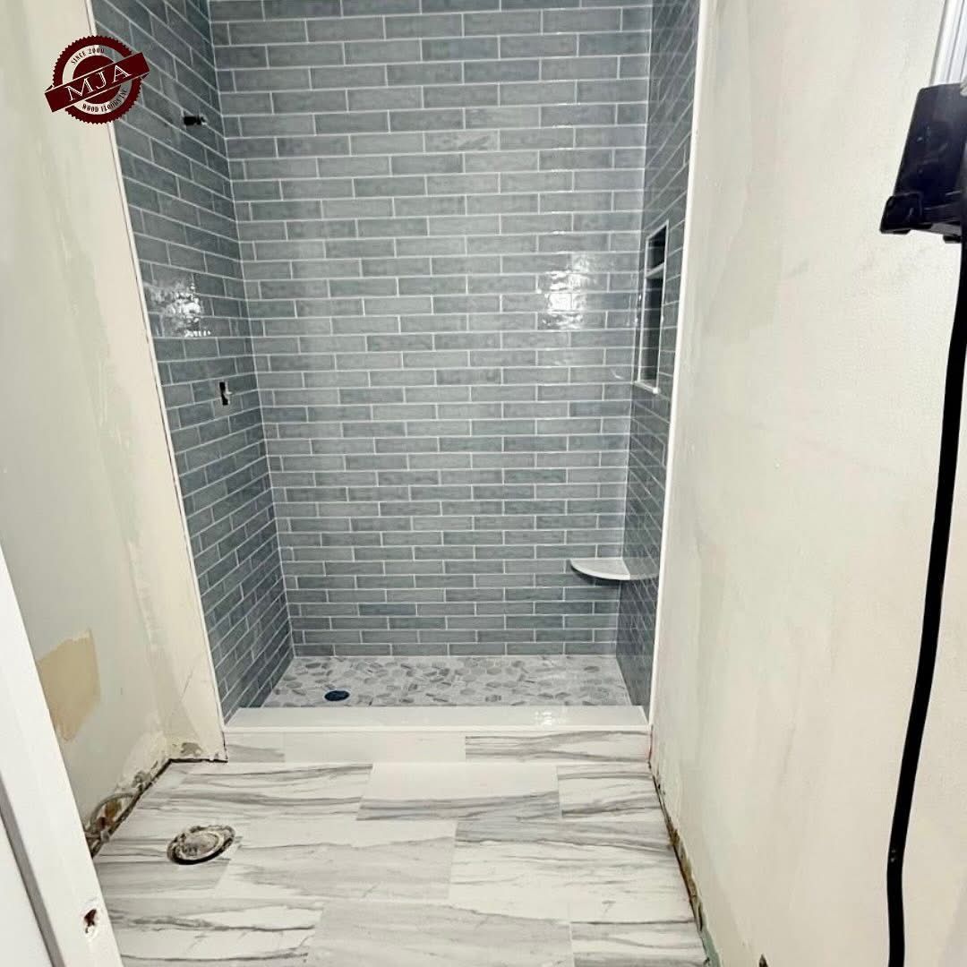 A bathroom undergoing renovation, featuring a walk-in shower with grey subway tile and white marble-patterned flooring.
