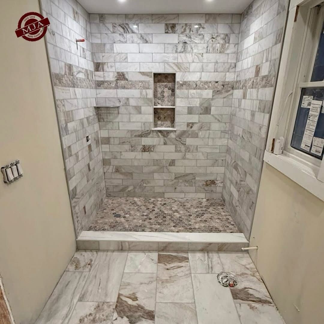 A walk-in shower with marble-look subway tile walls, a pebble-stone floor, and a two-tier recessed niche.