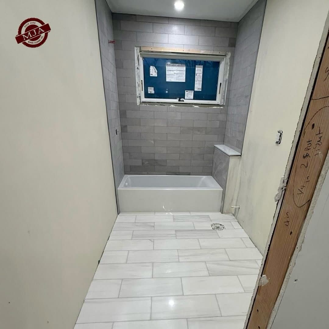 A bathroom under renovation with light gray subway-tiled walls, a white bathtub, and white marble-look floor tiles.
