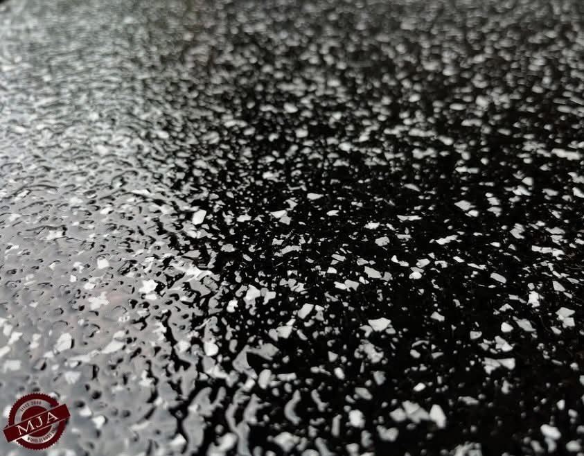 Close-up of a black textured surface with scattered white flecks, reflecting light with a slightly wet appearance.