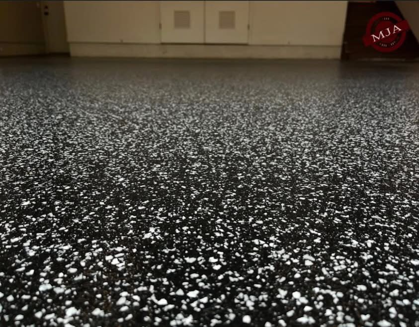 A close-up view of a garage floor featuring a black base coat speckled with white decorative flakes.