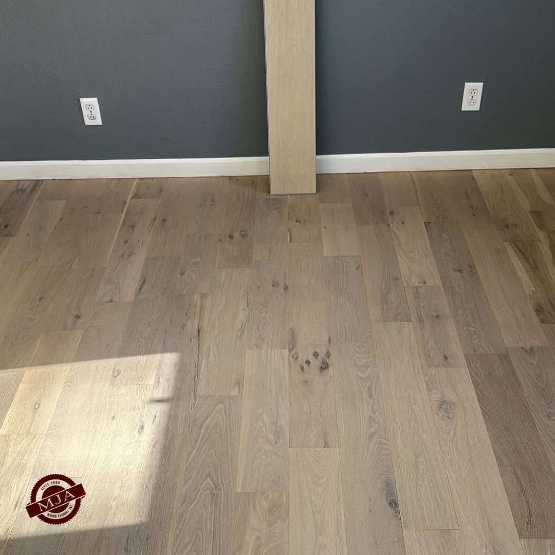 Wide-plank light wood flooring in a room with dark grey walls and white baseboards, with one loose plank standing upright.