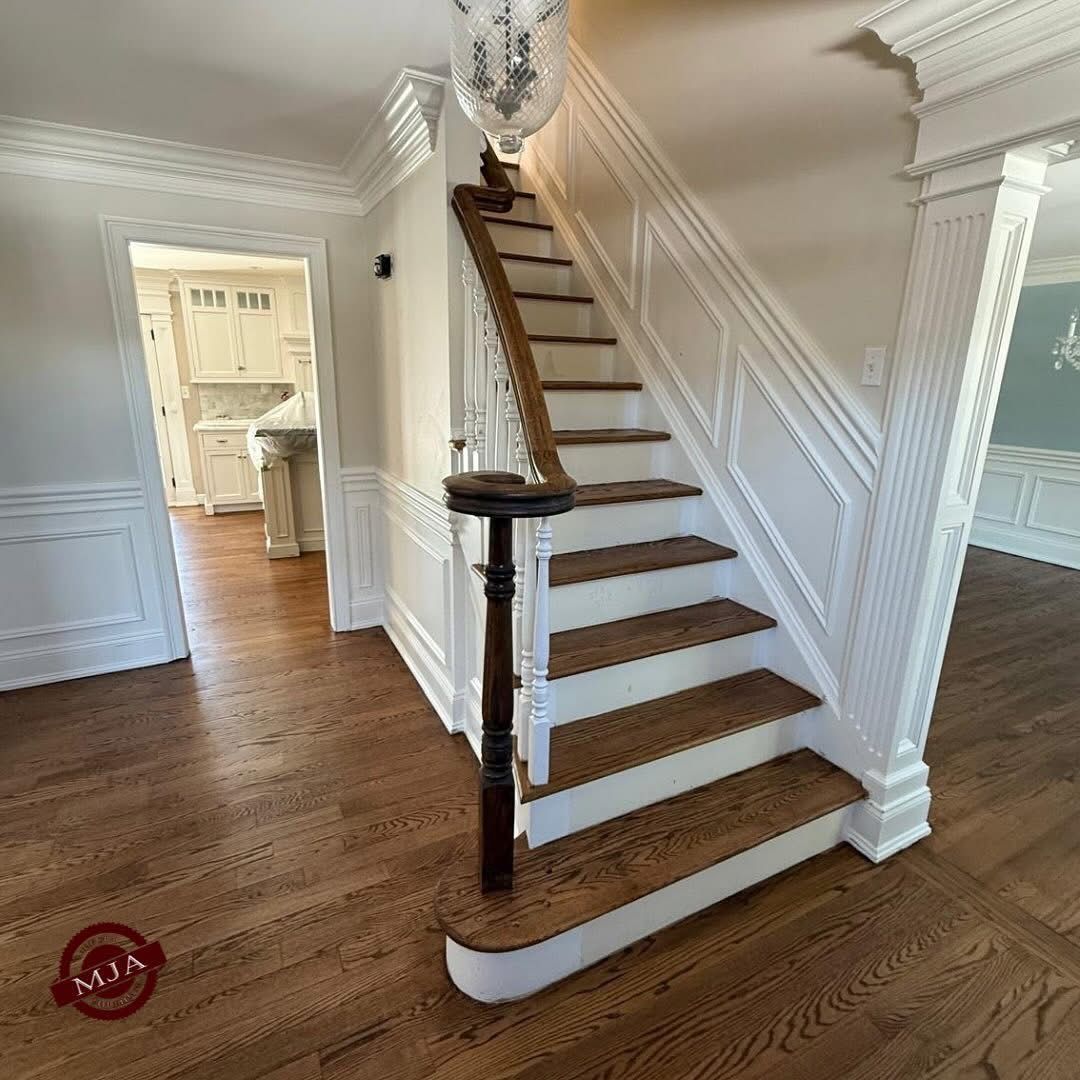 A wooden staircase with white risers and railings ascends in a bright foyer with hardwood floors and wall paneling.