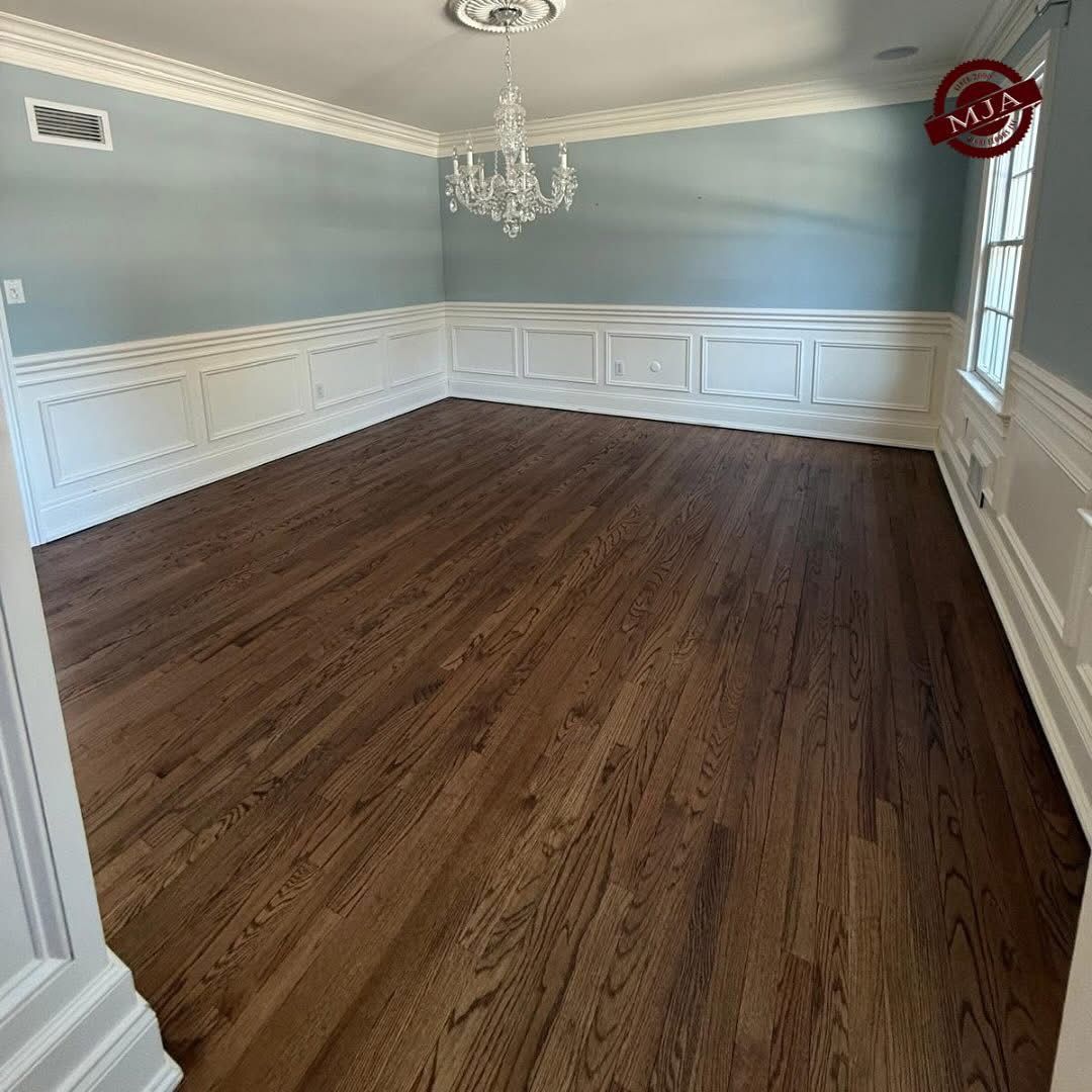 An empty room with dark wood flooring, light blue walls, white wainscoting, and a crystal chandelier.