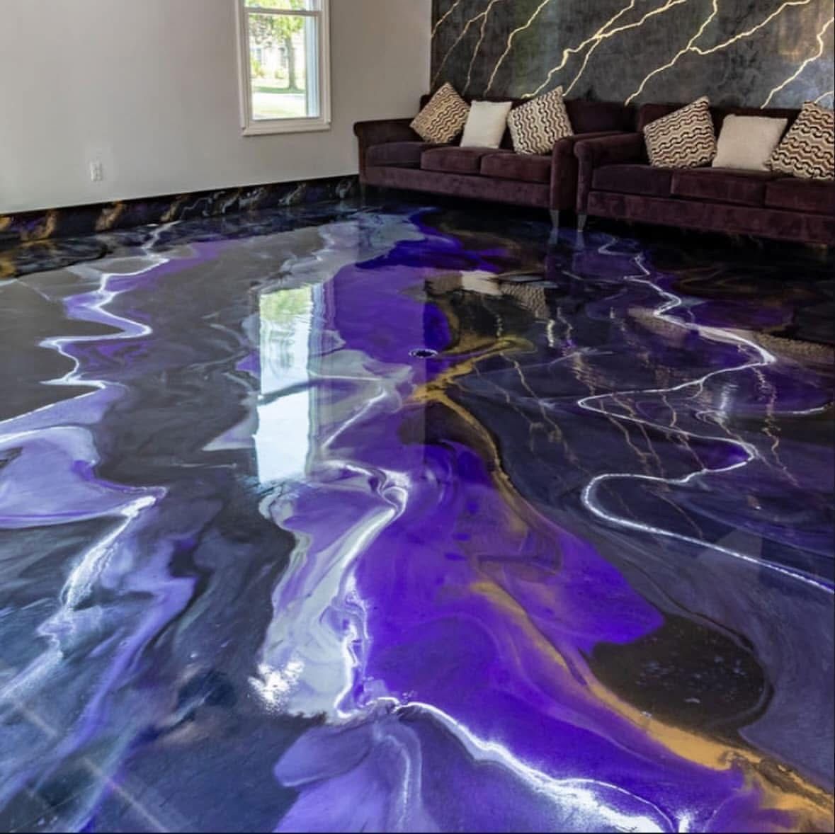 A living room with a purple, black, and gold marble-patterned epoxy floor and matching accent wall behind a dark sofa.