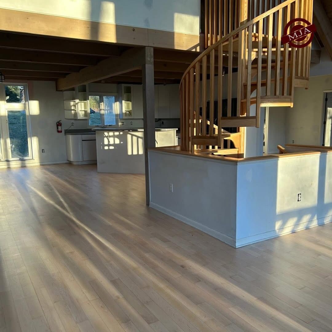 Modern open-concept living space with light wood floors, a white kitchen island, and a wooden spiral staircase.