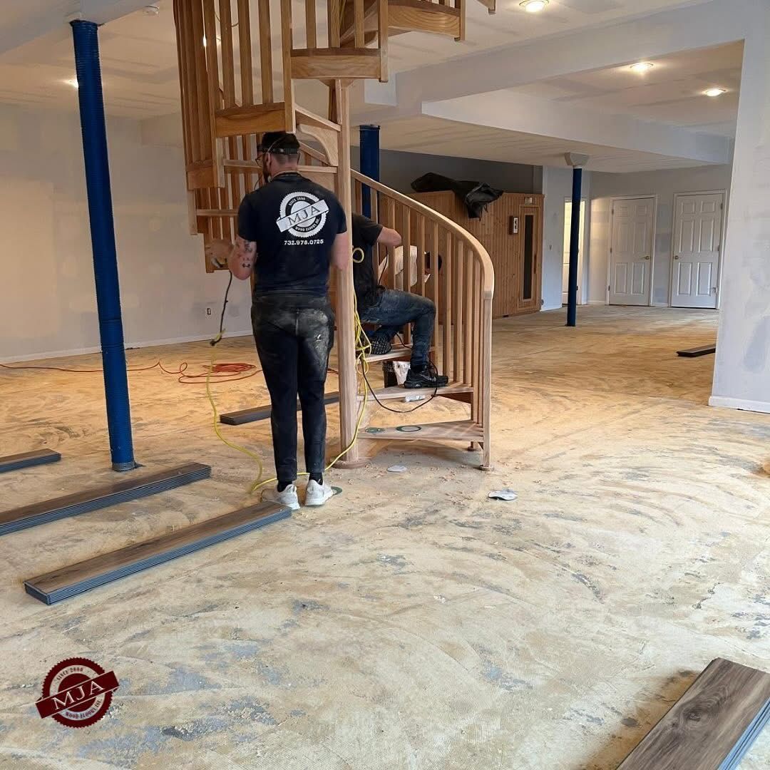 Two people working on a wood spiral staircase inside a room under construction with bare floors.