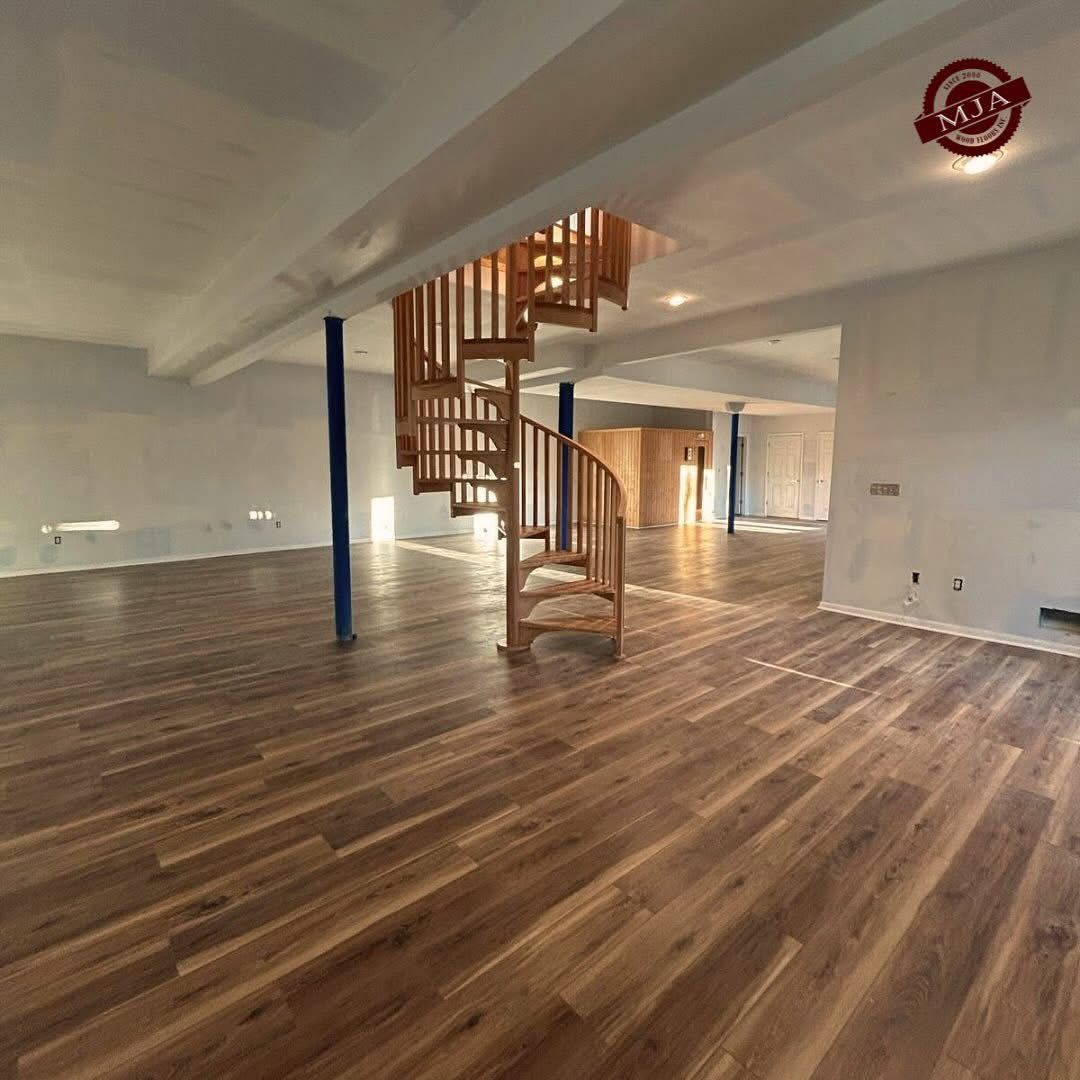 An open basement featuring light-colored walls, wood-grain flooring, structural blue pillars, and a spiral staircase.