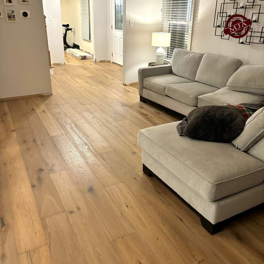 A living room with light hardwood floors, a gray sectional sofa, a table lamp, and a modern wall art piece.