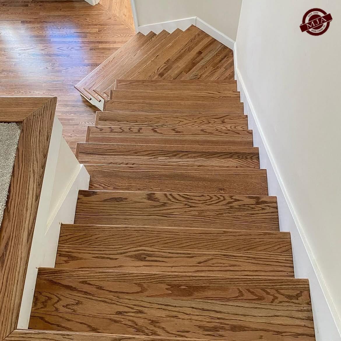 A top-down view of wooden stairs descending from a landing, featuring light-colored walls and wood-patterned flooring.