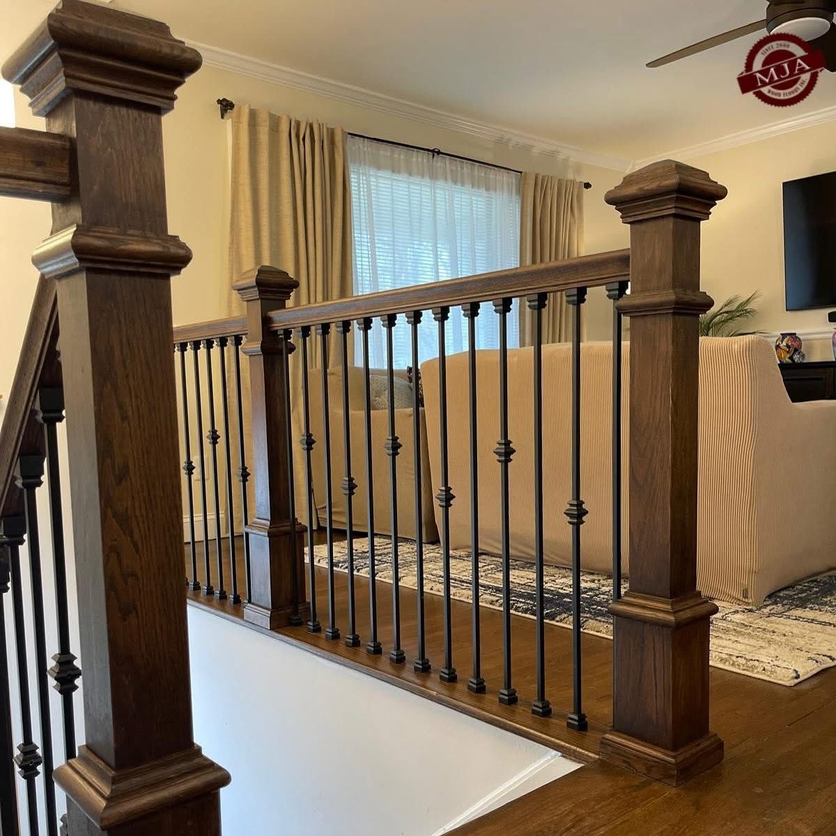 A wooden staircase railing with dark wood posts and black metal balusters overlooking a living room.