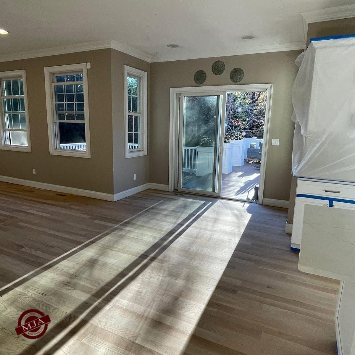 A bright, modern room featuring light wood floors, tan walls, large windows, and a glass sliding door leading outdoors.