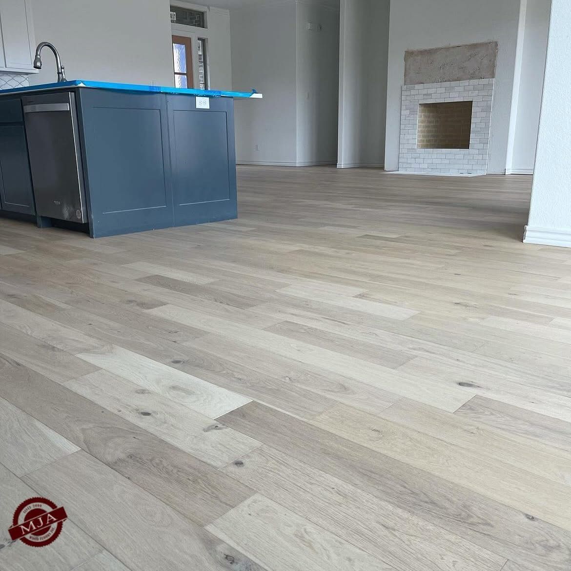 Light-colored hardwood flooring installed in a kitchen with a blue island and a fireplace in the background.