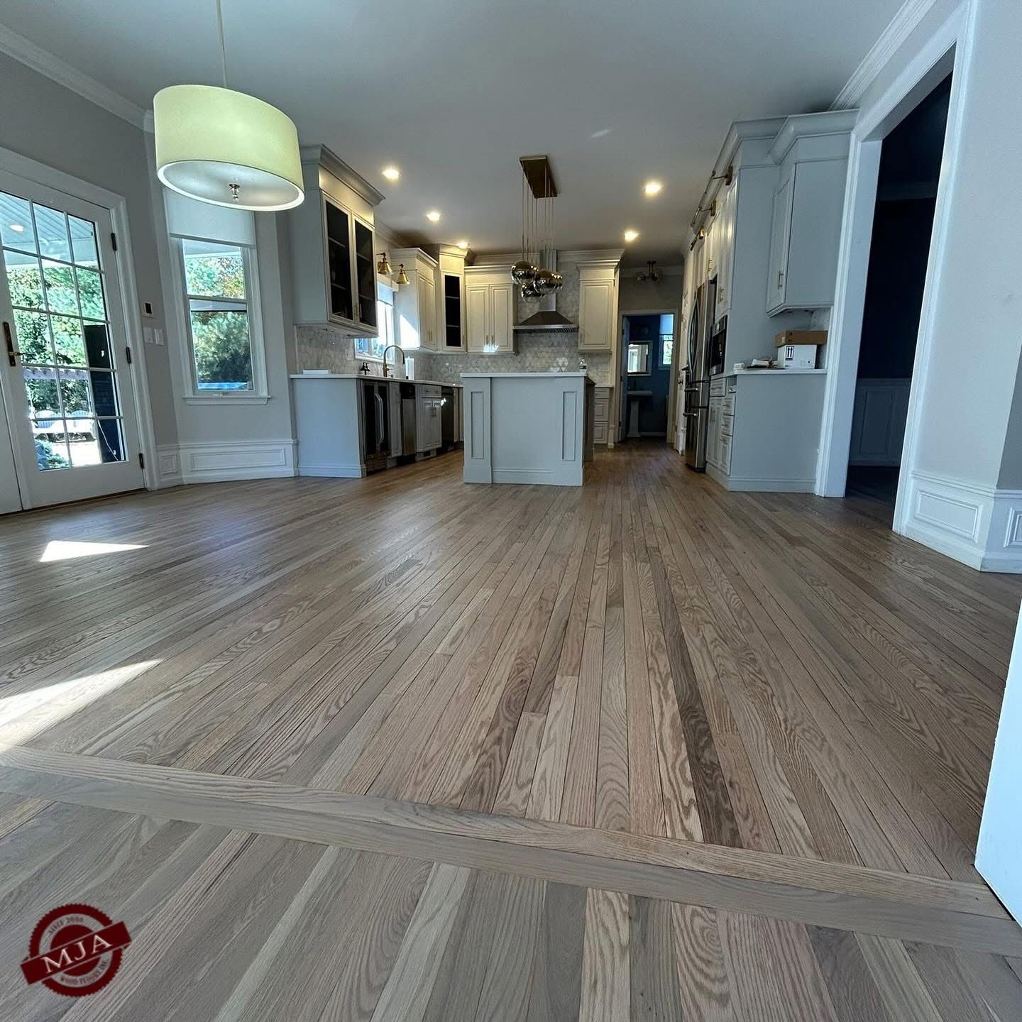 A wide-angle view of a modern kitchen with light wood floors, grey cabinetry, a central island, and a pendant light.